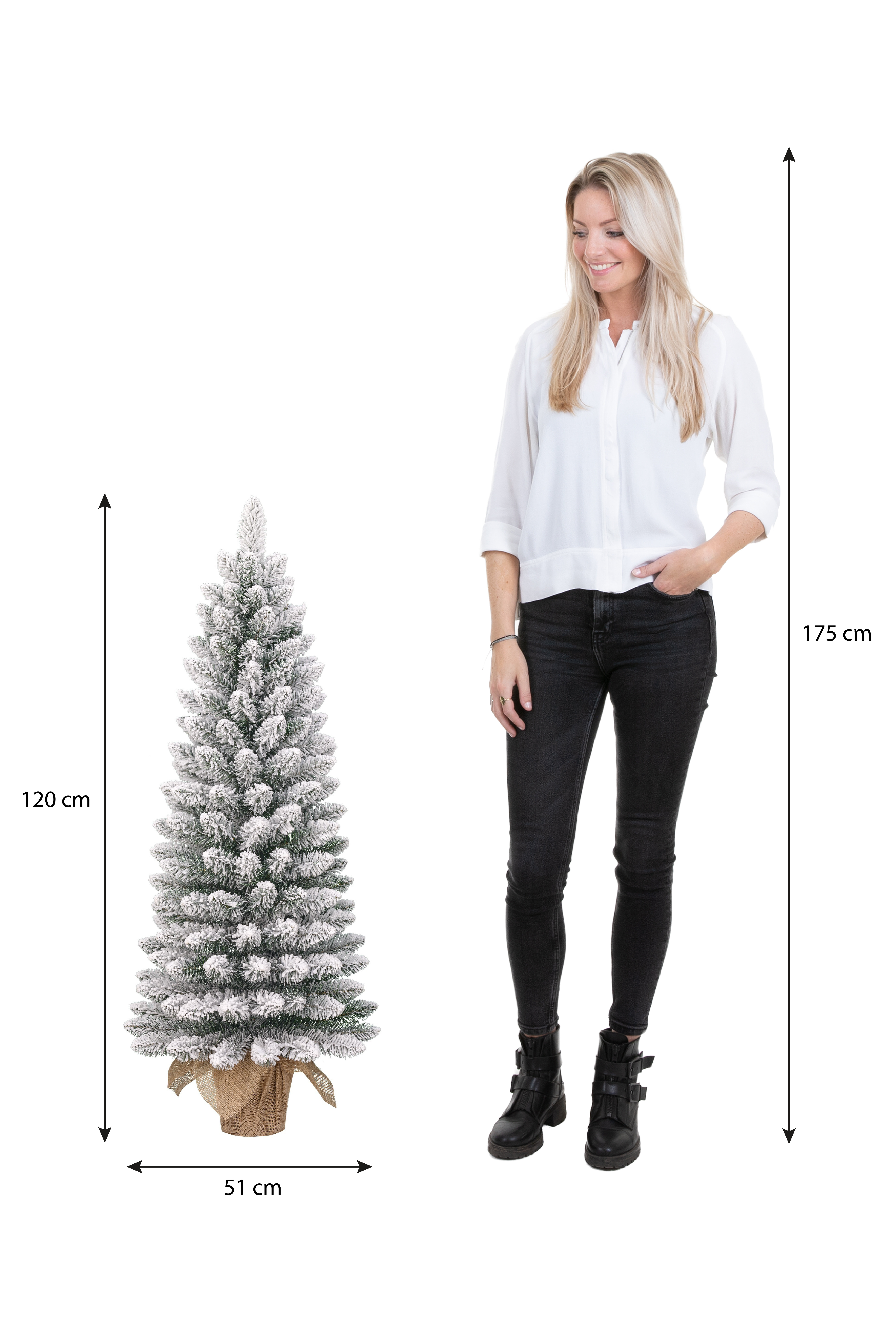 Une femme se tient près d'un sapin de Noël. L'arbre est recouvert de neige. Les dimensions sont affichées. La femme porte une chemise blanche et un jean noir.
