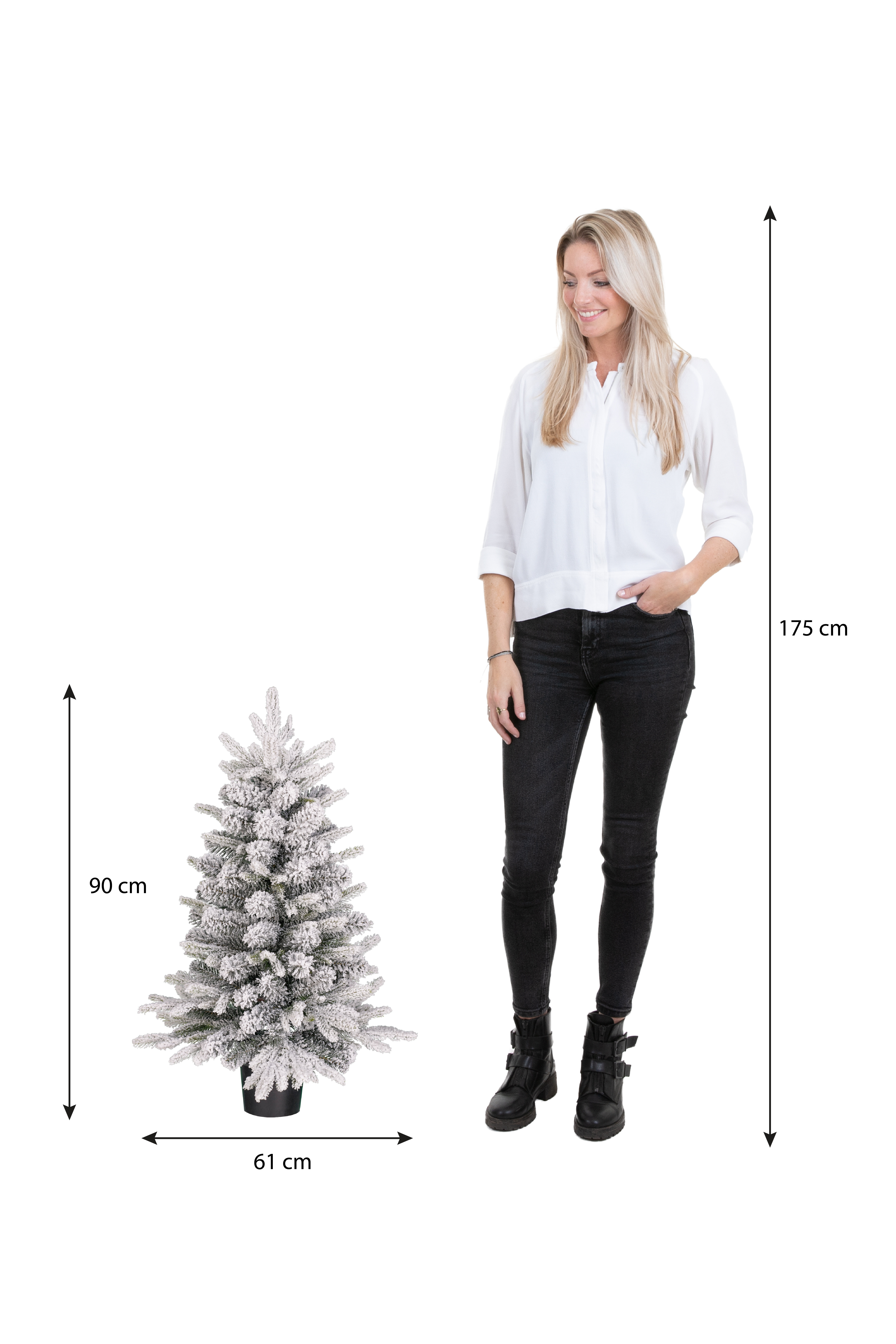 Een vrouw staat naast een kleine, met sneeuw bedekte kerstboom. De vrouw is lang en lacht. Afmetingen worden aangegeven.