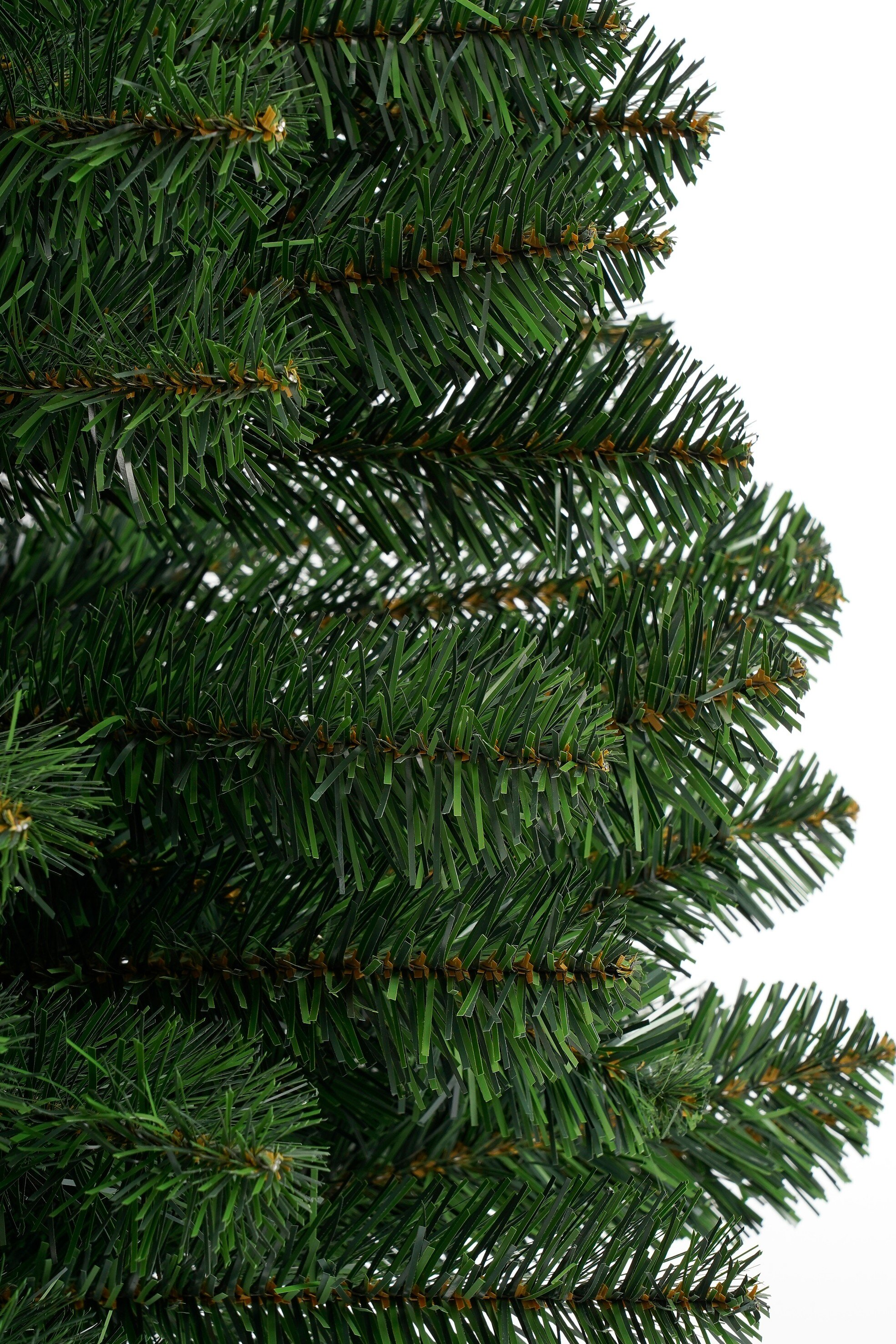 Gros plan d'une branche verte artificielle de sapin de Noël sur fond blanc.