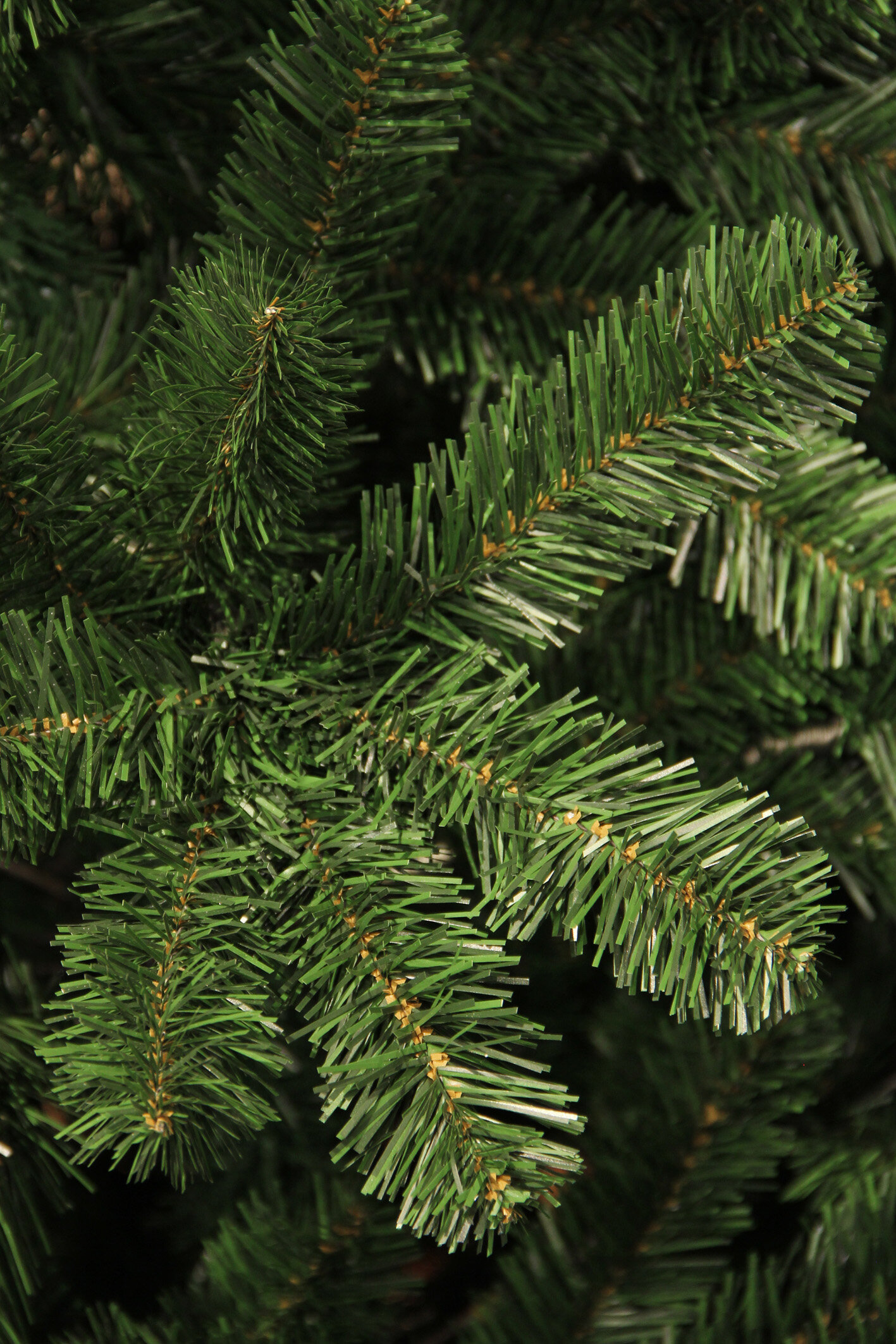 Gros plan sur des branches de sapin artificielles vertes. Les aiguilles sont courtes et denses. Le fond est vert foncé, flou.