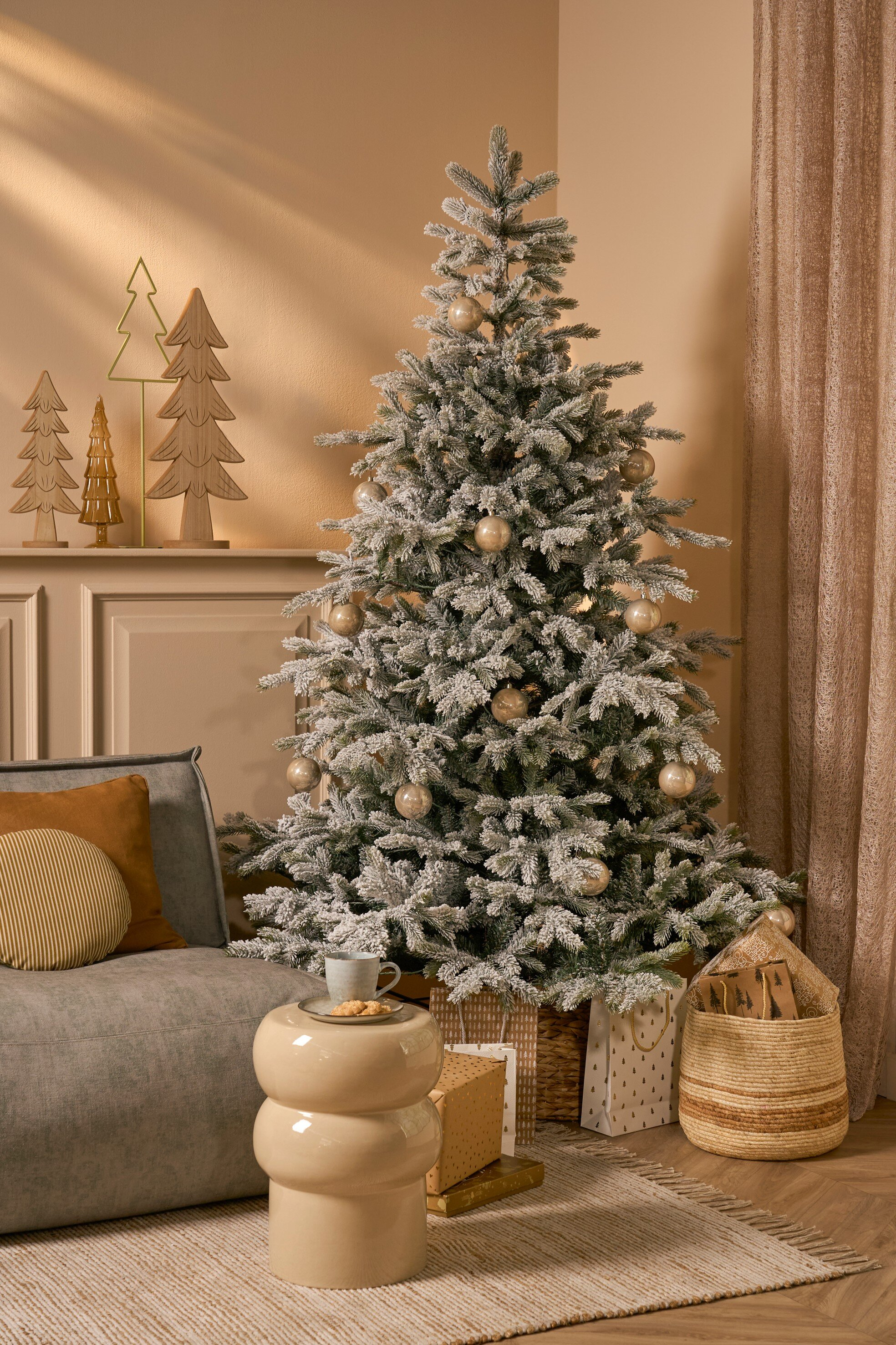 Un sapin de Noël décoré près d'un canapé. Une table avec une tasse et des biscuits devant.