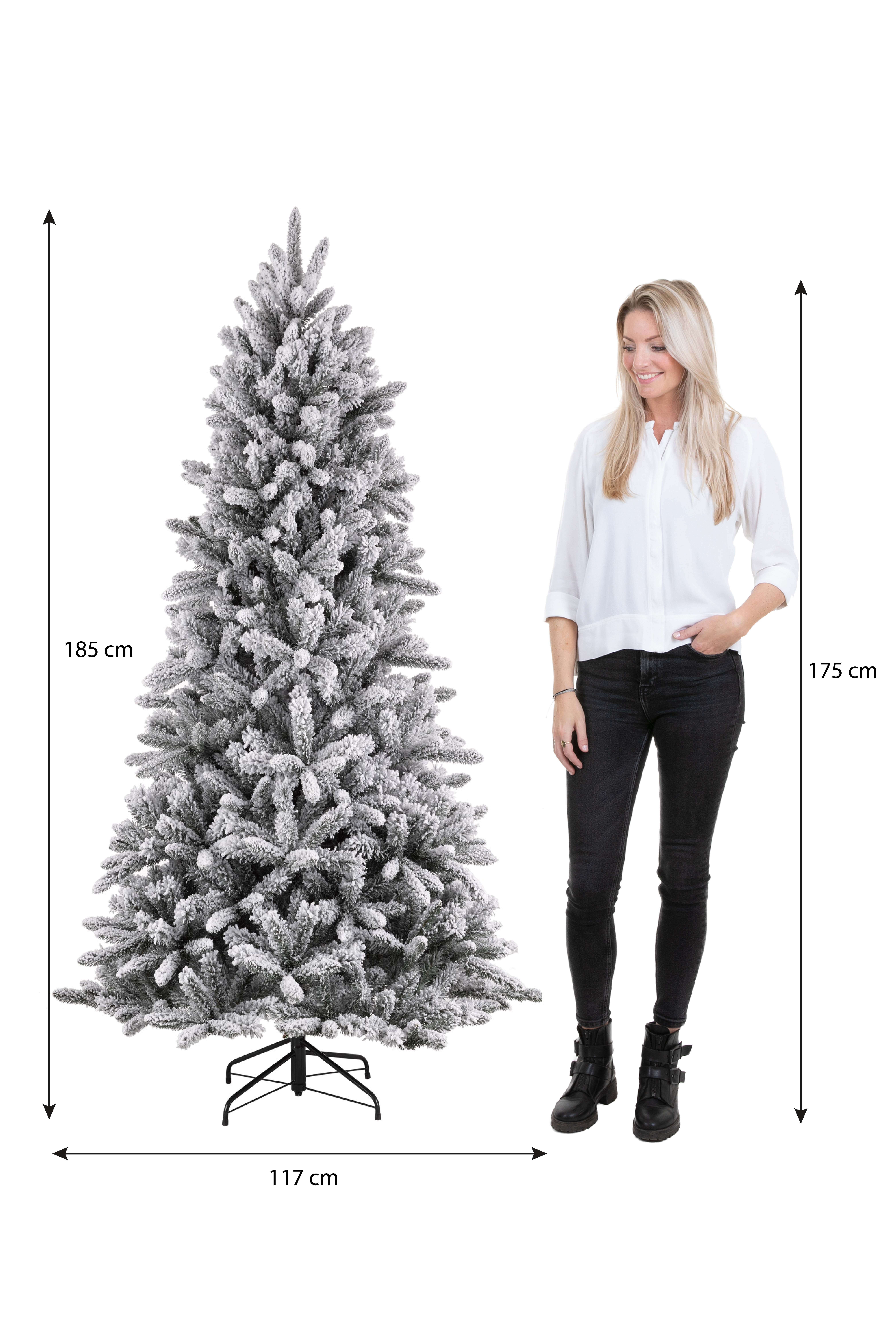 Une femme se tient près d'un sapin de Noël enneigé. Des mesures sont indiquées sur le côté, l'arbre mesure 185 cm de haut et 117 cm de large.