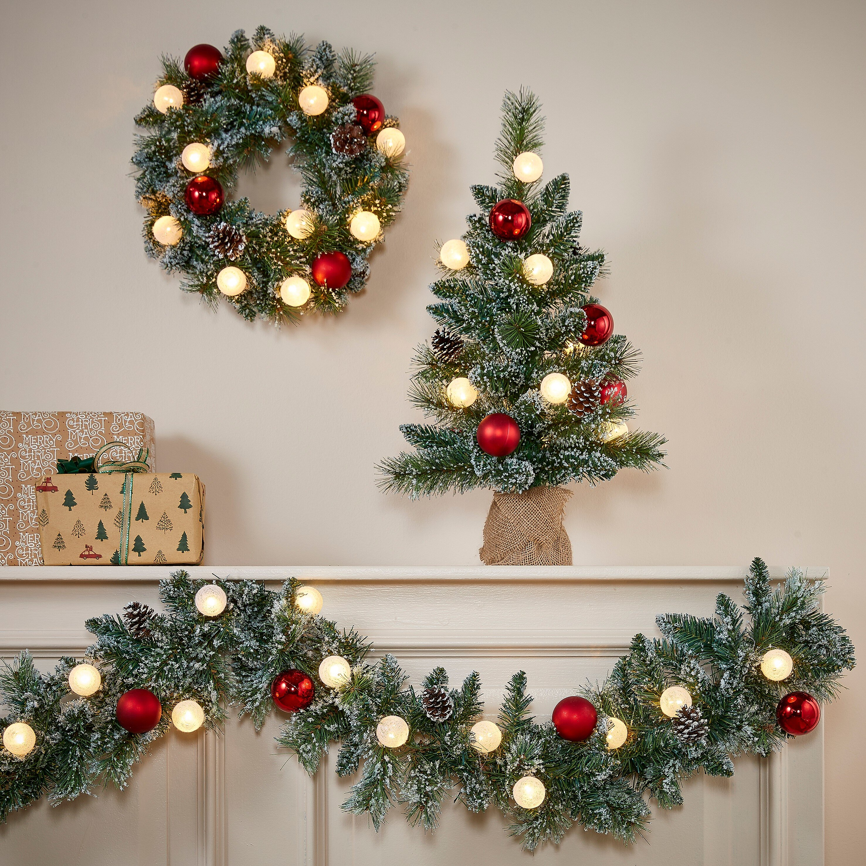 Une scène de Noël avec une couronne, un arbre et une guirlande. Des ornements rouges et des lumières décorent.