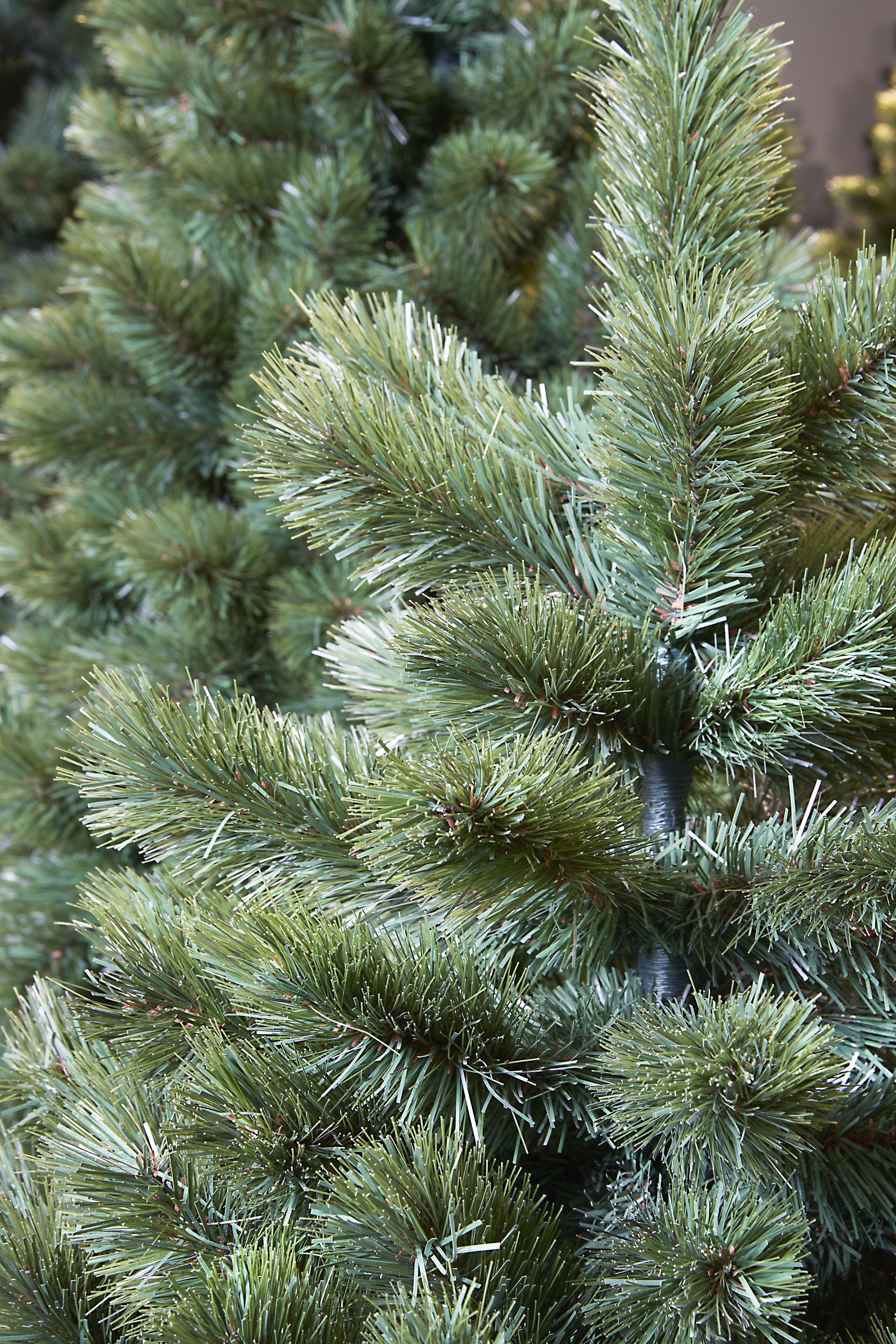 Gros plan sur un sapin de Noël artificiel vert. Les aiguilles sont denses et détaillées, avec une légère teinte bleue.