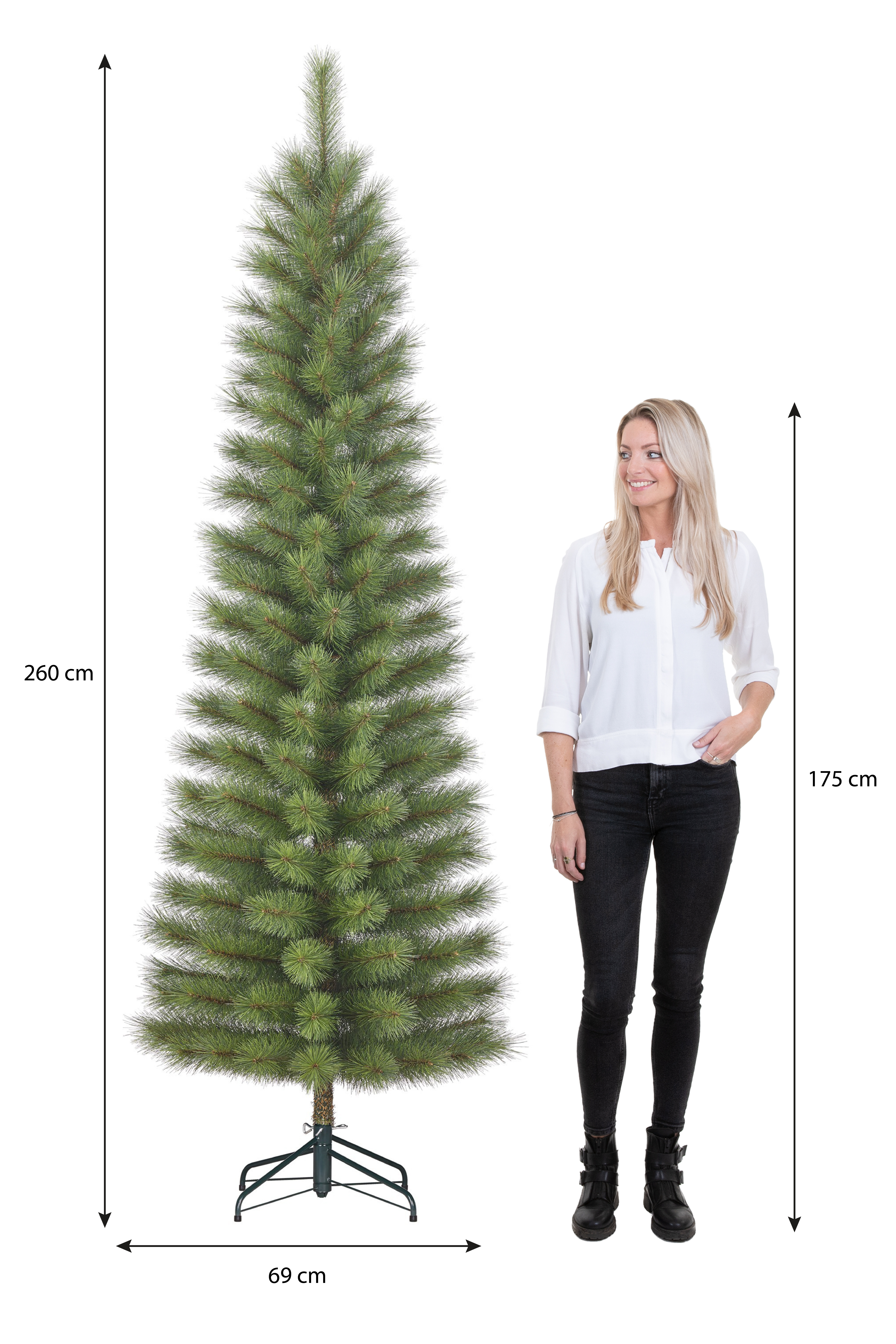 Un grand sapin de Noël vert se tient à côté d'une femme en chemise blanche et pantalon noir.