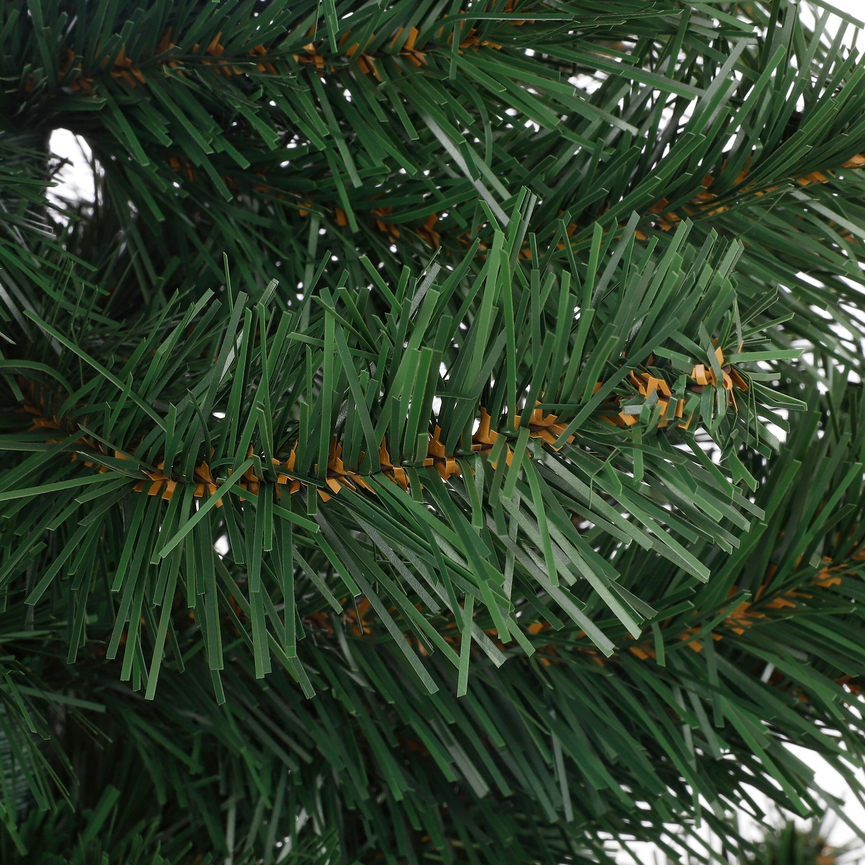Close-up van een groene kunstkerstboomtak. De naalden zijn lang en plat met bruine accenten.