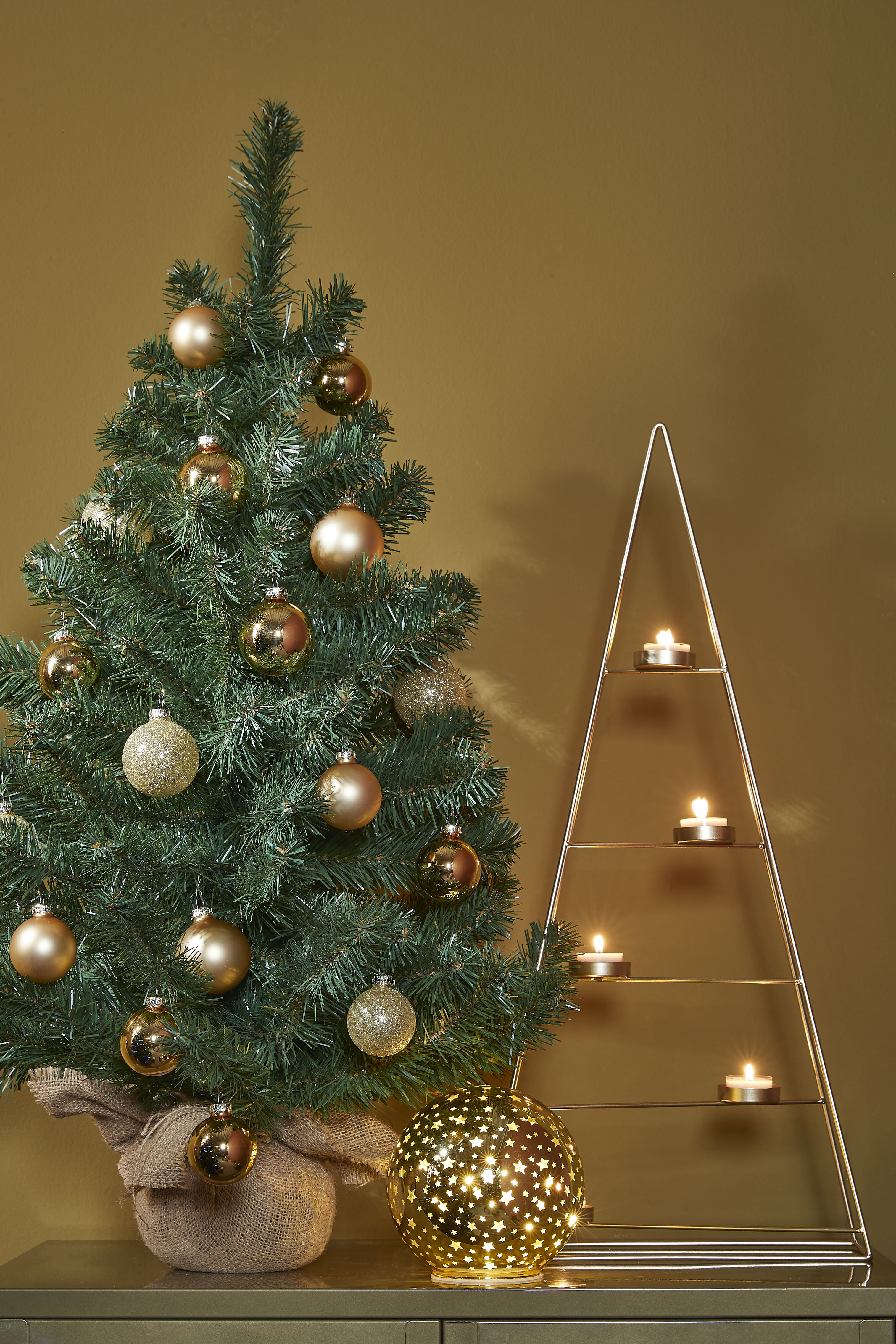 Een kerstboom met ornamenten. Een kandelaar en een stervormige lamp staan in de buurt. De achtergrond is geel.
