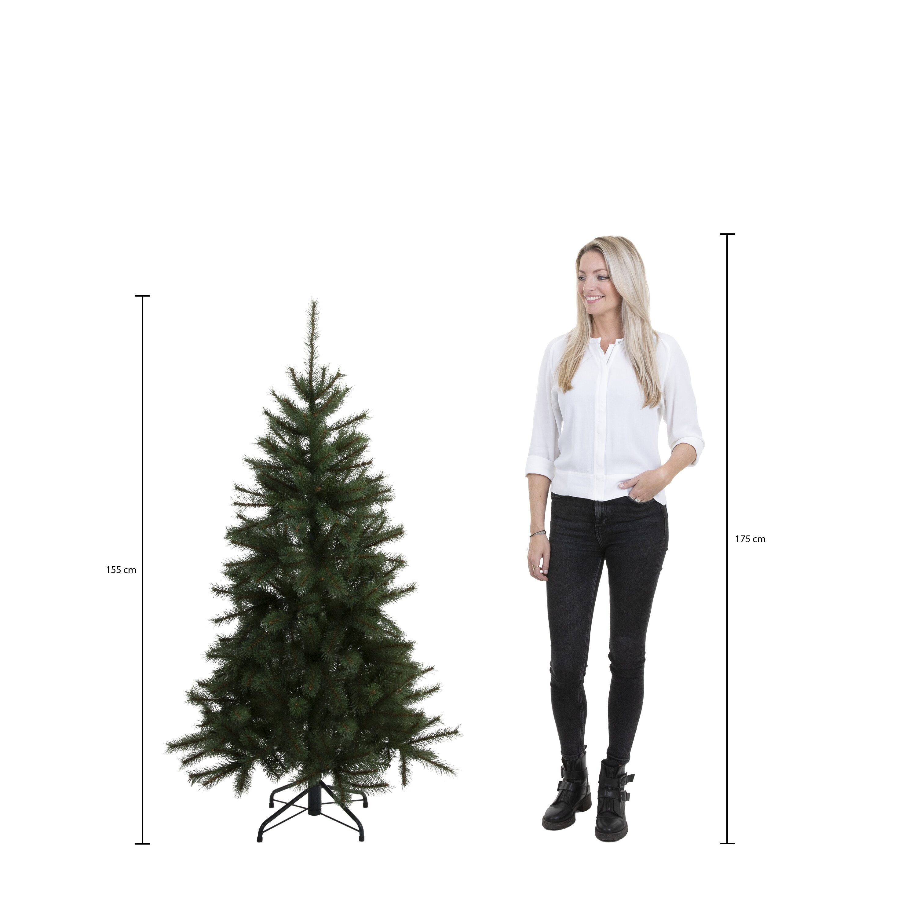 Une femme se tient près d'un sapin de Noël vert. Des mesures sont indiquées. La femme porte un pantalon et des bottes noirs.