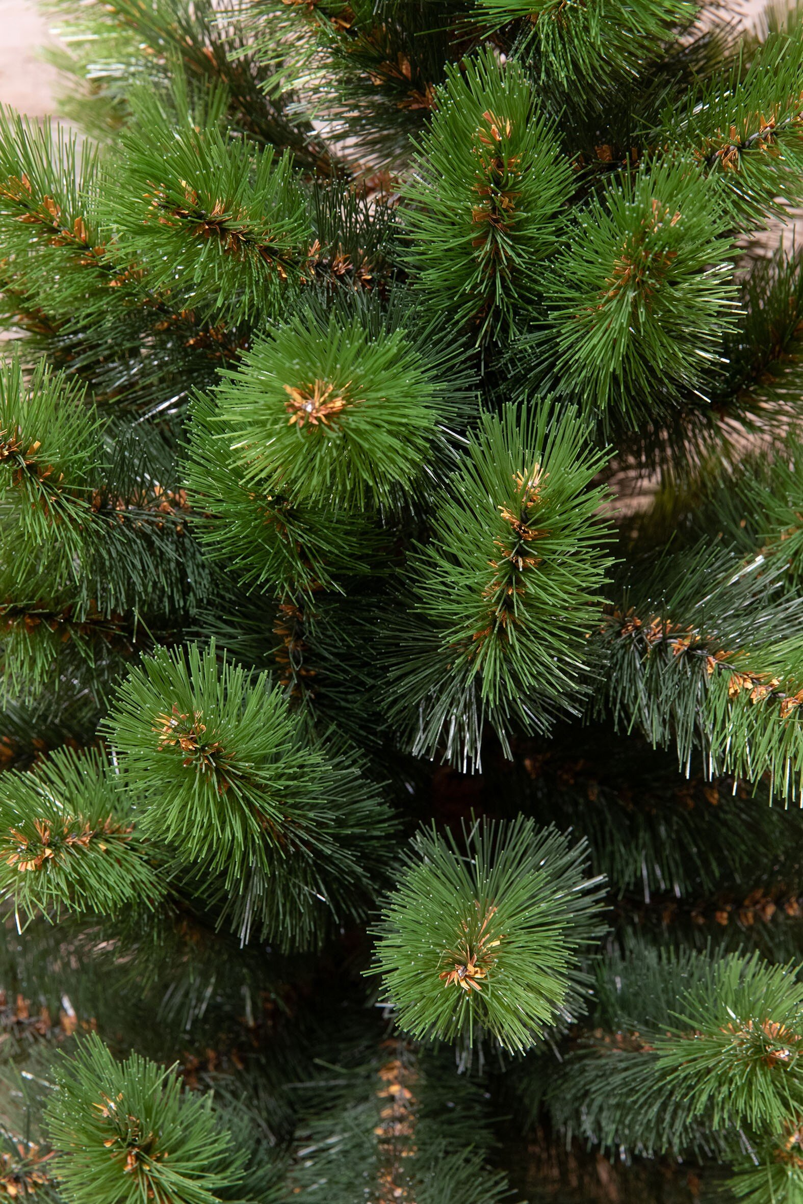Gros plan sur un sapin de Noël artificiel vert. Les aiguilles sont denses et groupées, avec des pointes marron.
