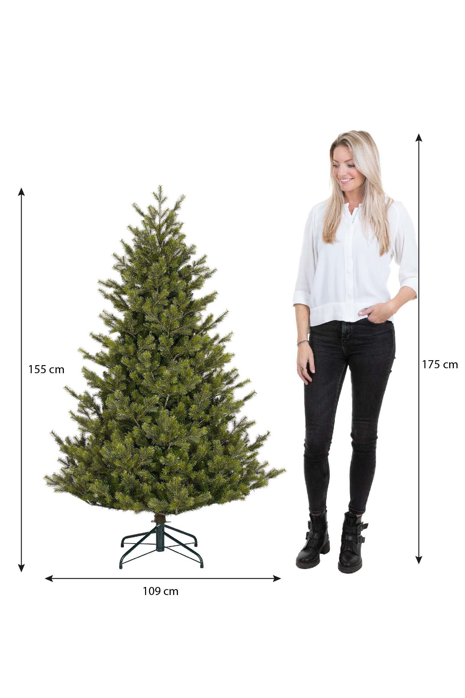Une femme se tient à côté d'un sapin de Noël vert. L'arbre mesure 155 cm de haut et 109 cm de large. La femme mesure 175 cm.