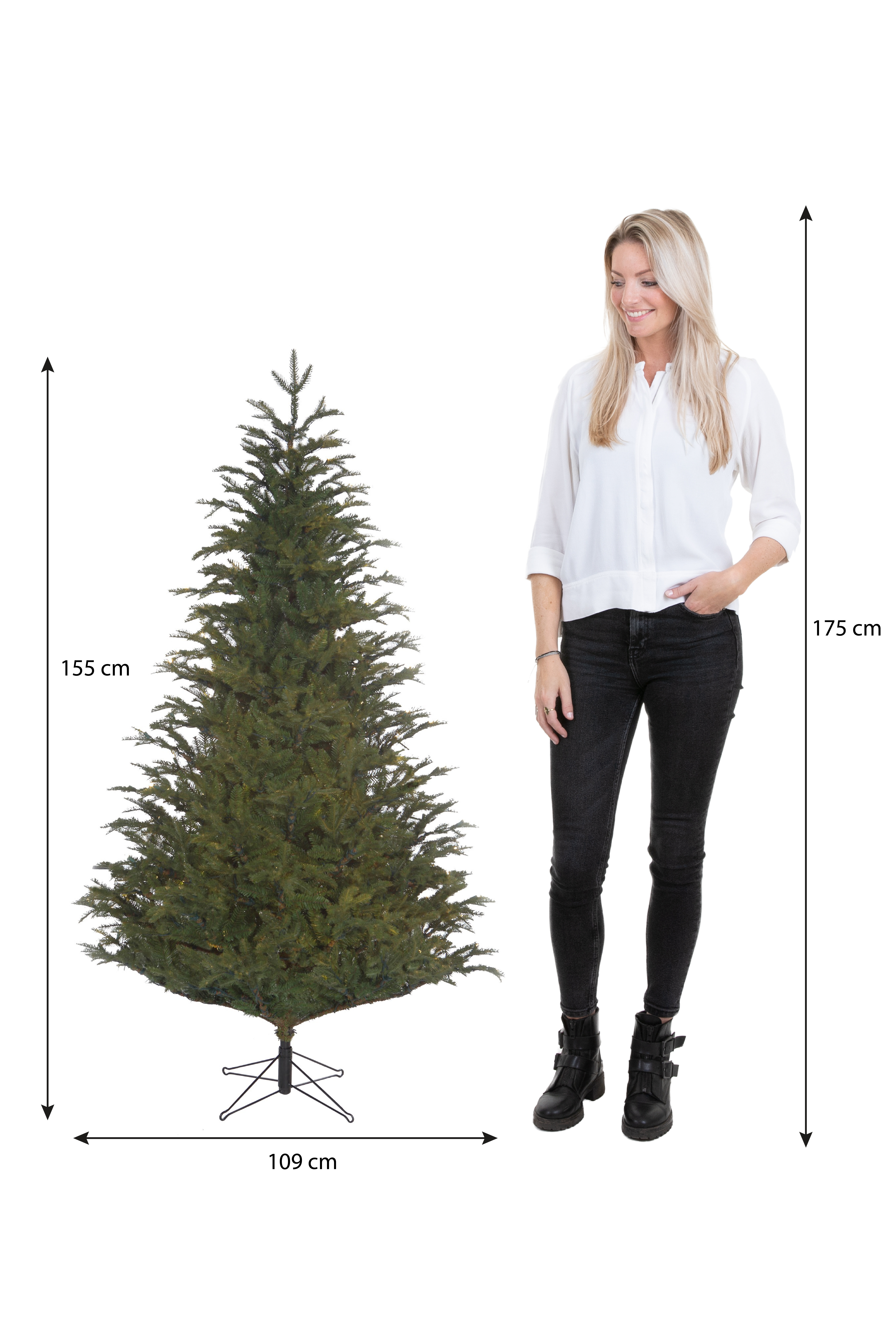 Une femme se tient à côté d'un sapin de Noël. L'arbre mesure 155 cm de haut et 109 cm de large. La femme mesure 175 cm.
