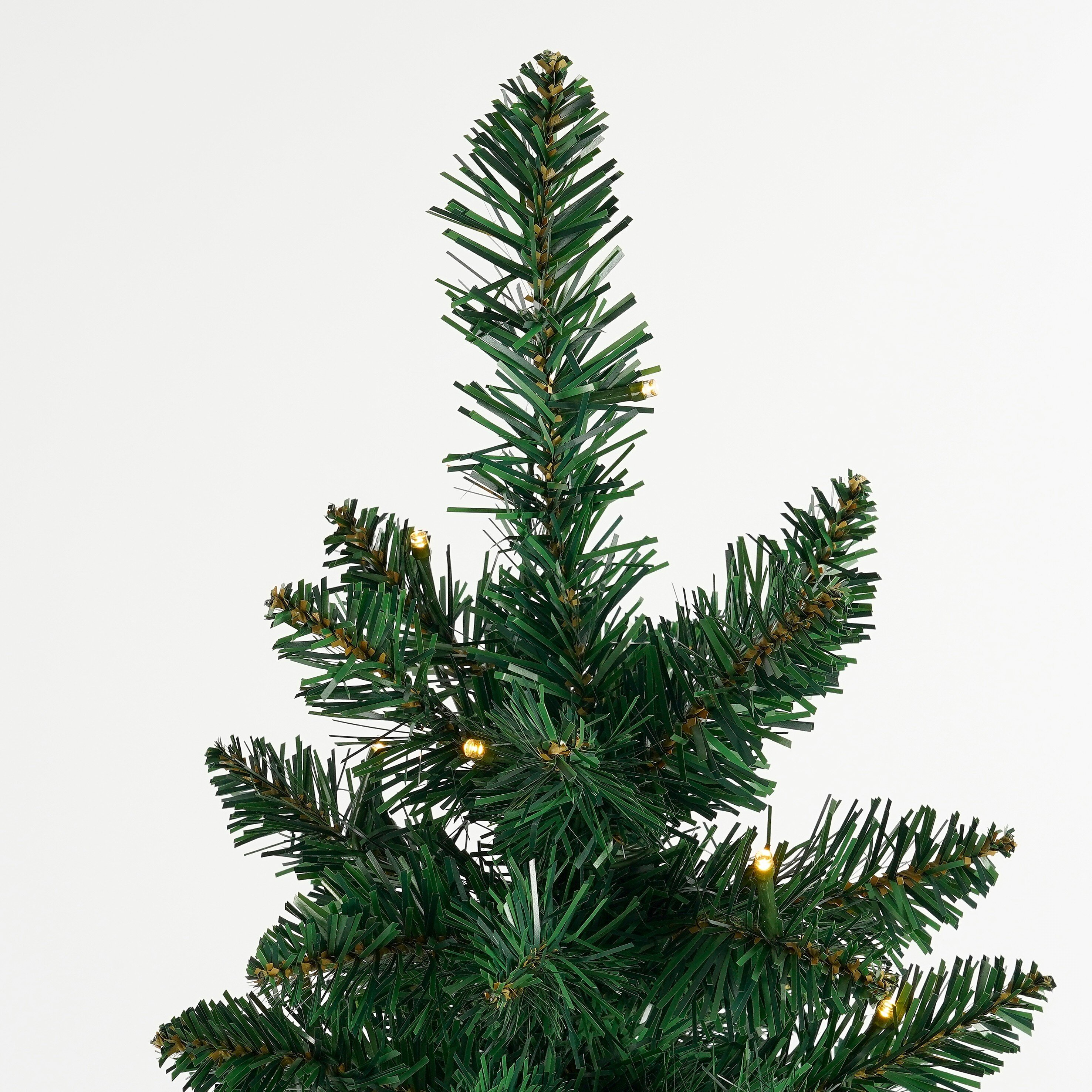 Gros plan d'un sapin de Noël artificiel vert avec de petites lumières jaunes sur fond blanc.
