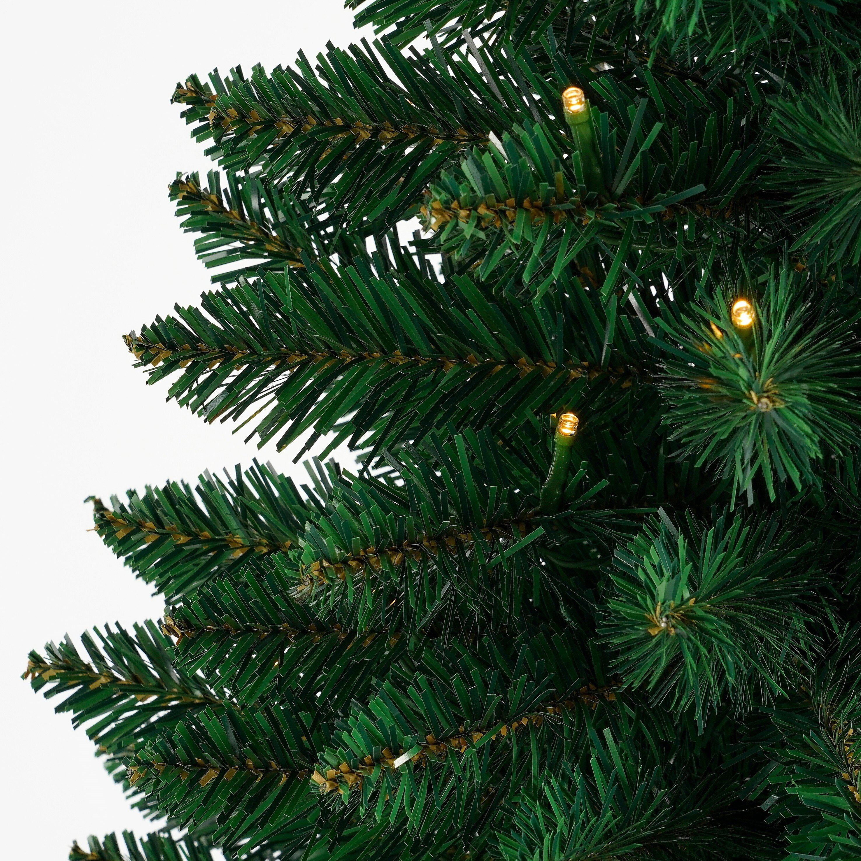 Gros plan d'un sapin de Noël avec des aiguilles vertes et de petites lumières jaunes, sur fond blanc.