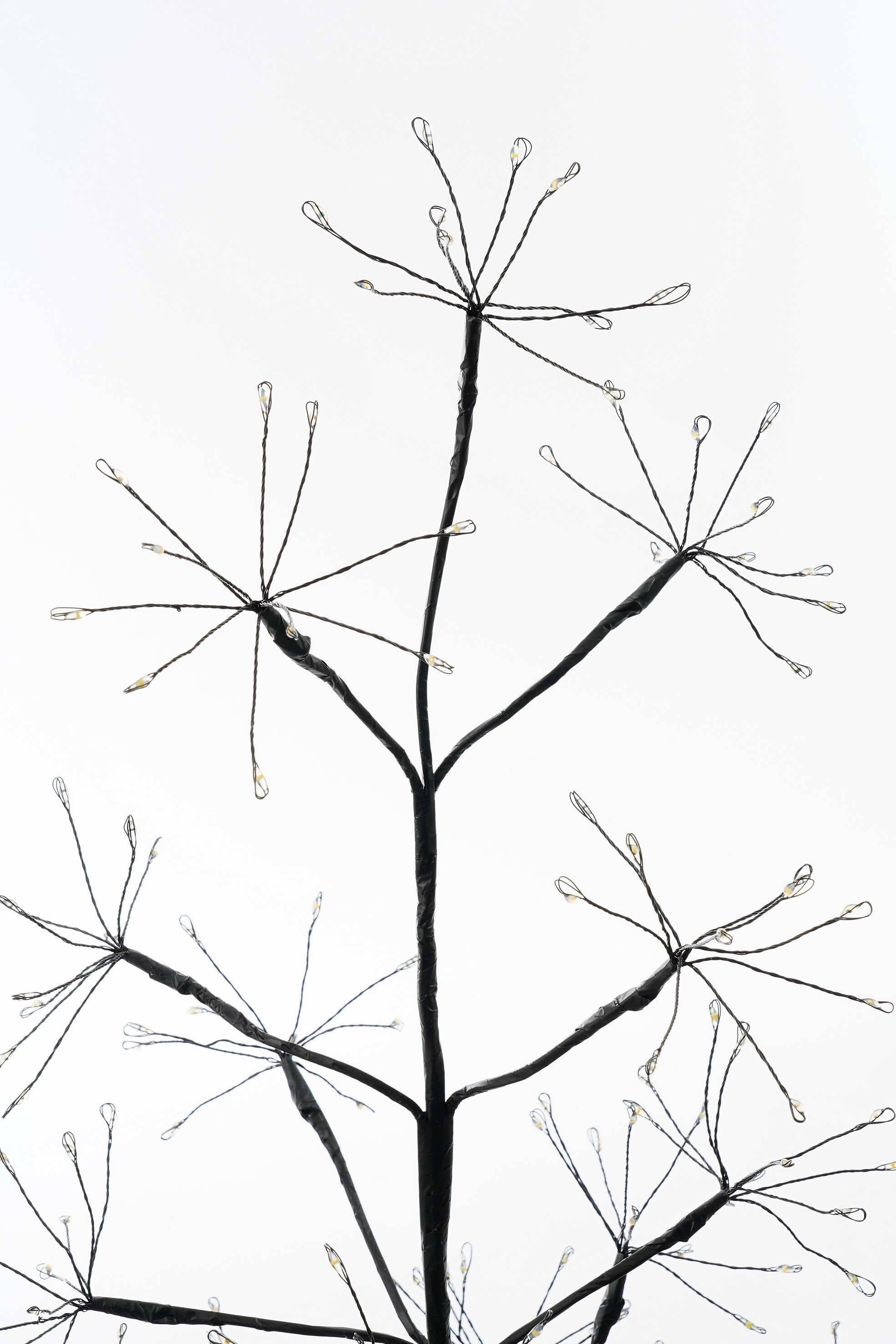 Un arbre décoratif avec des branches noires et de petites lumières sur fond blanc.