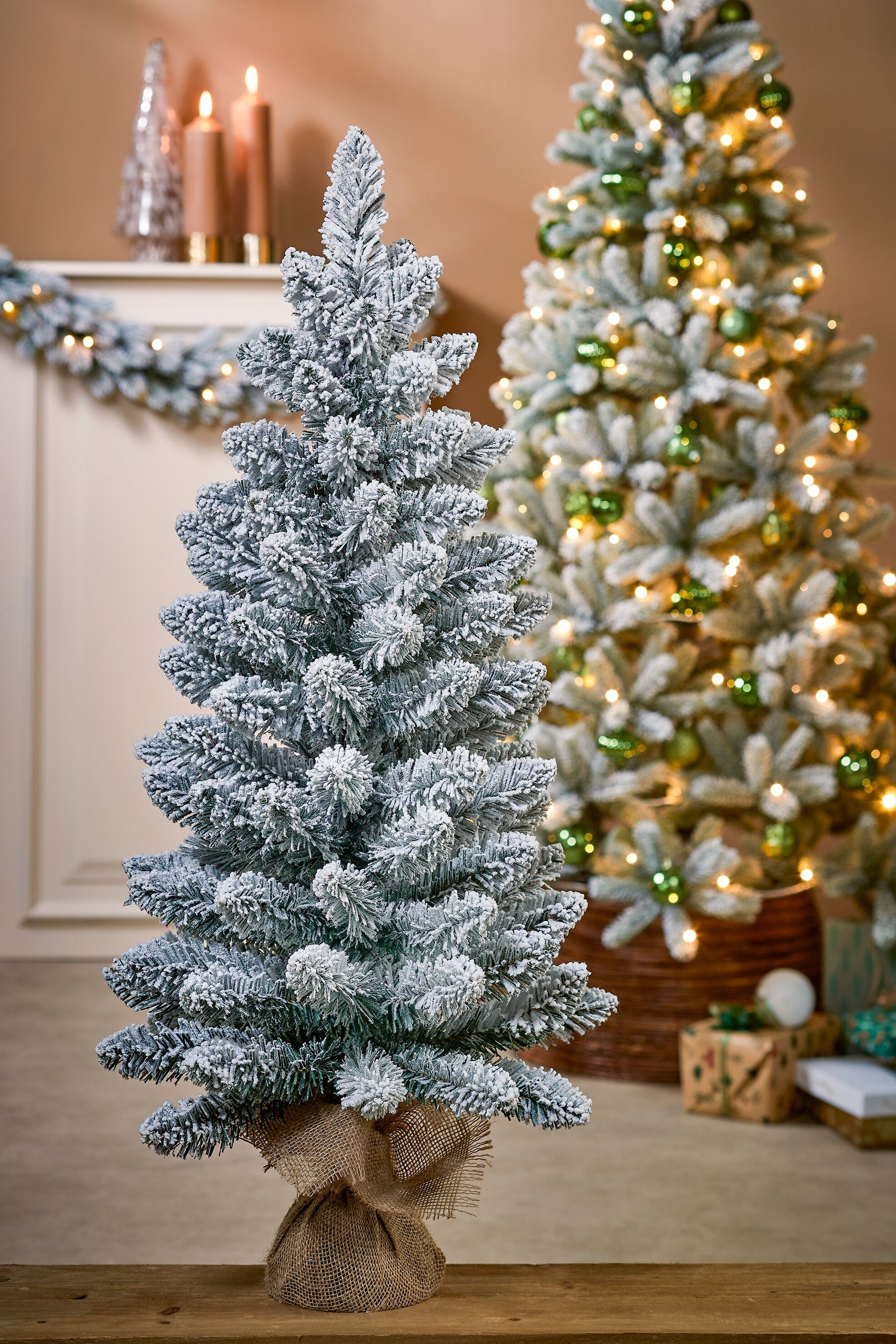 Un sapin de Noël floqué est mis au point, un autre en arrière-plan. Ornements, bougies et cadeaux sont visibles.