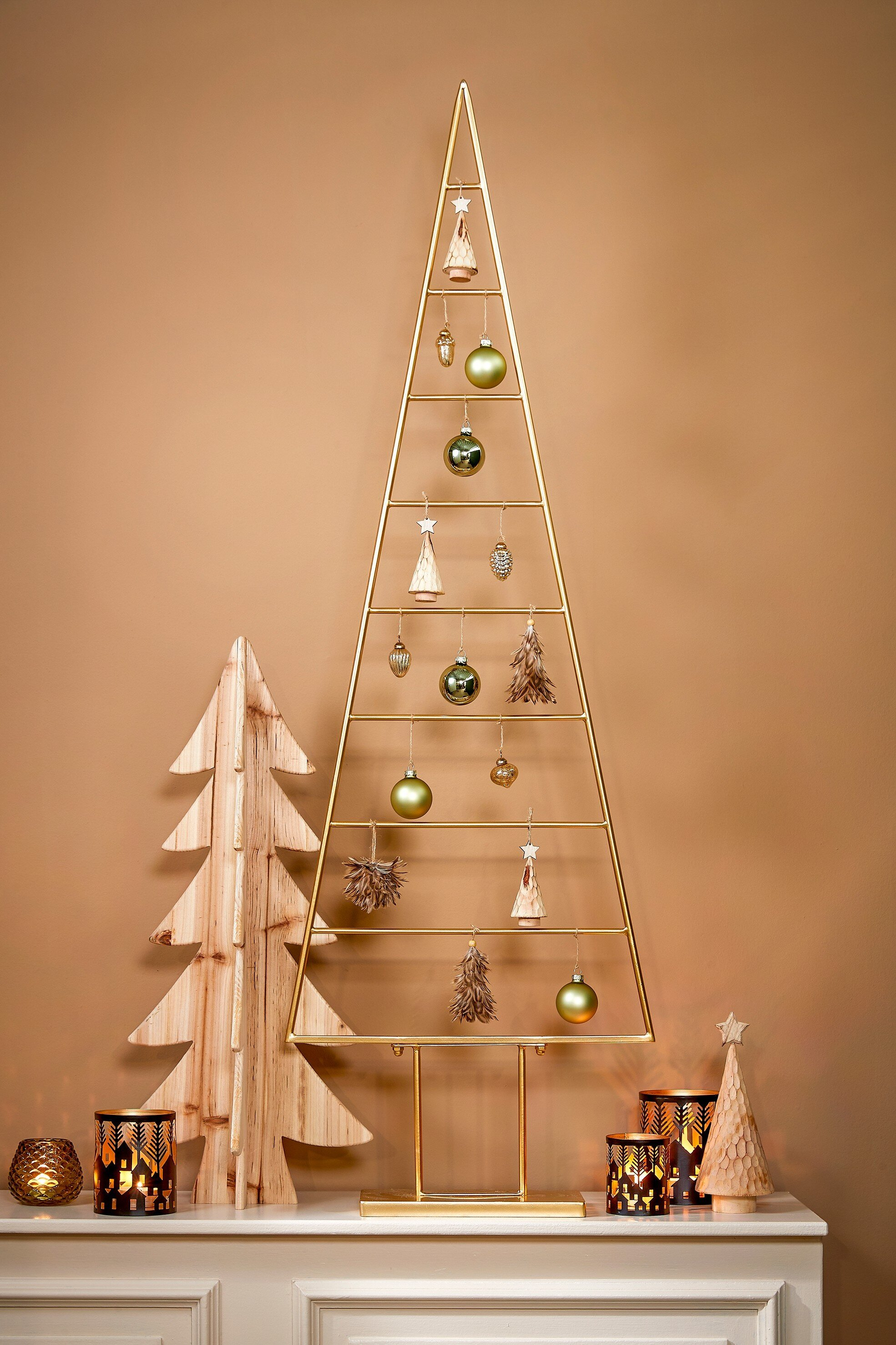 Un sapin de Noël doré est décoré d'ornements. Des arbres en bois et des bougeoirs sur une surface blanche.