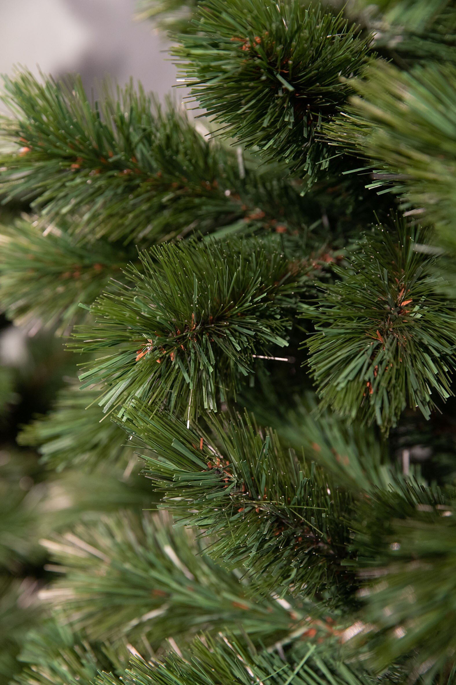 Gros plan sur un sapin de Noël artificiel vert. Les aiguilles sont détaillées et superposées, avec un fond clair.