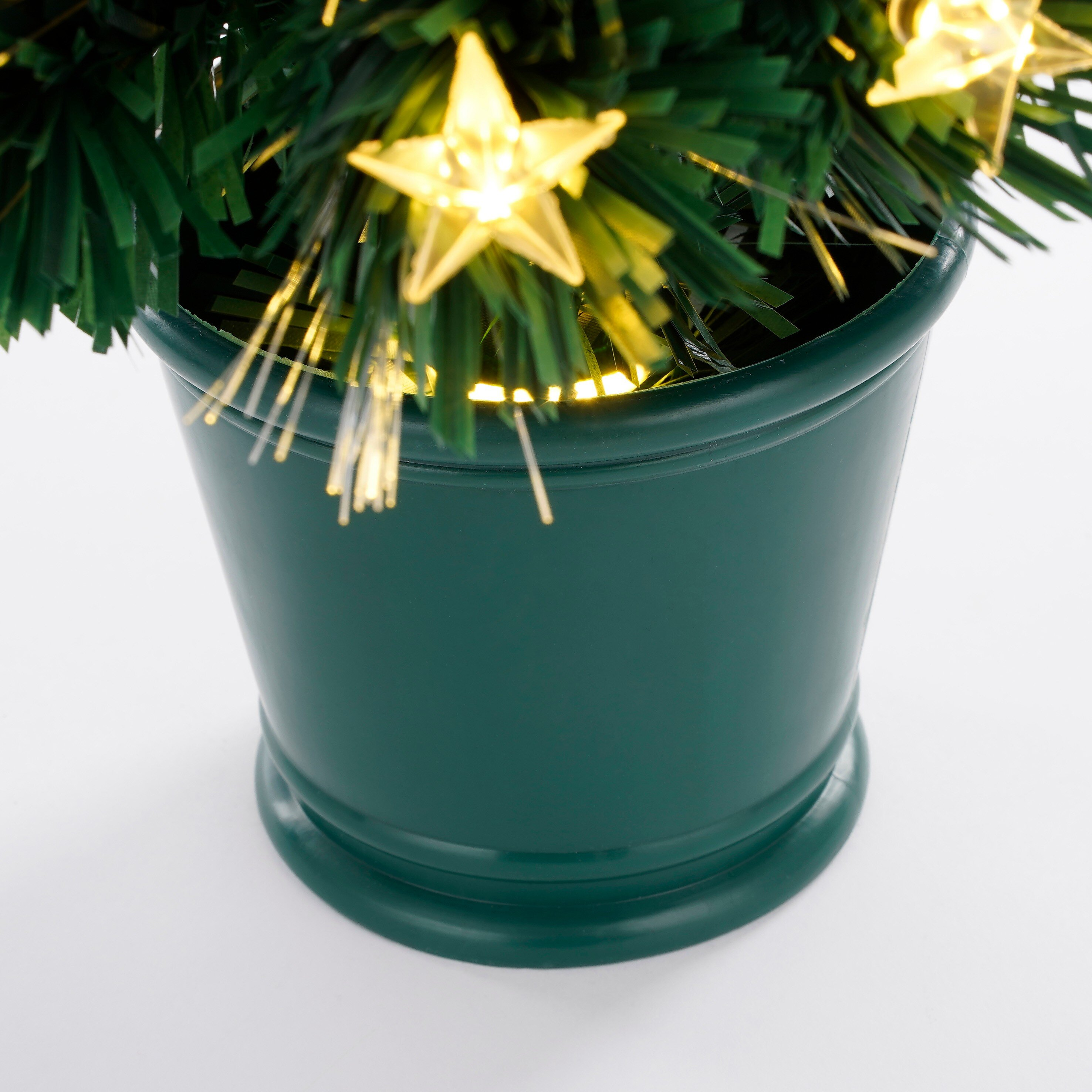 Een kleine groene kerstboom in pot met stervormige lichtjes, tegen een witte achtergrond.