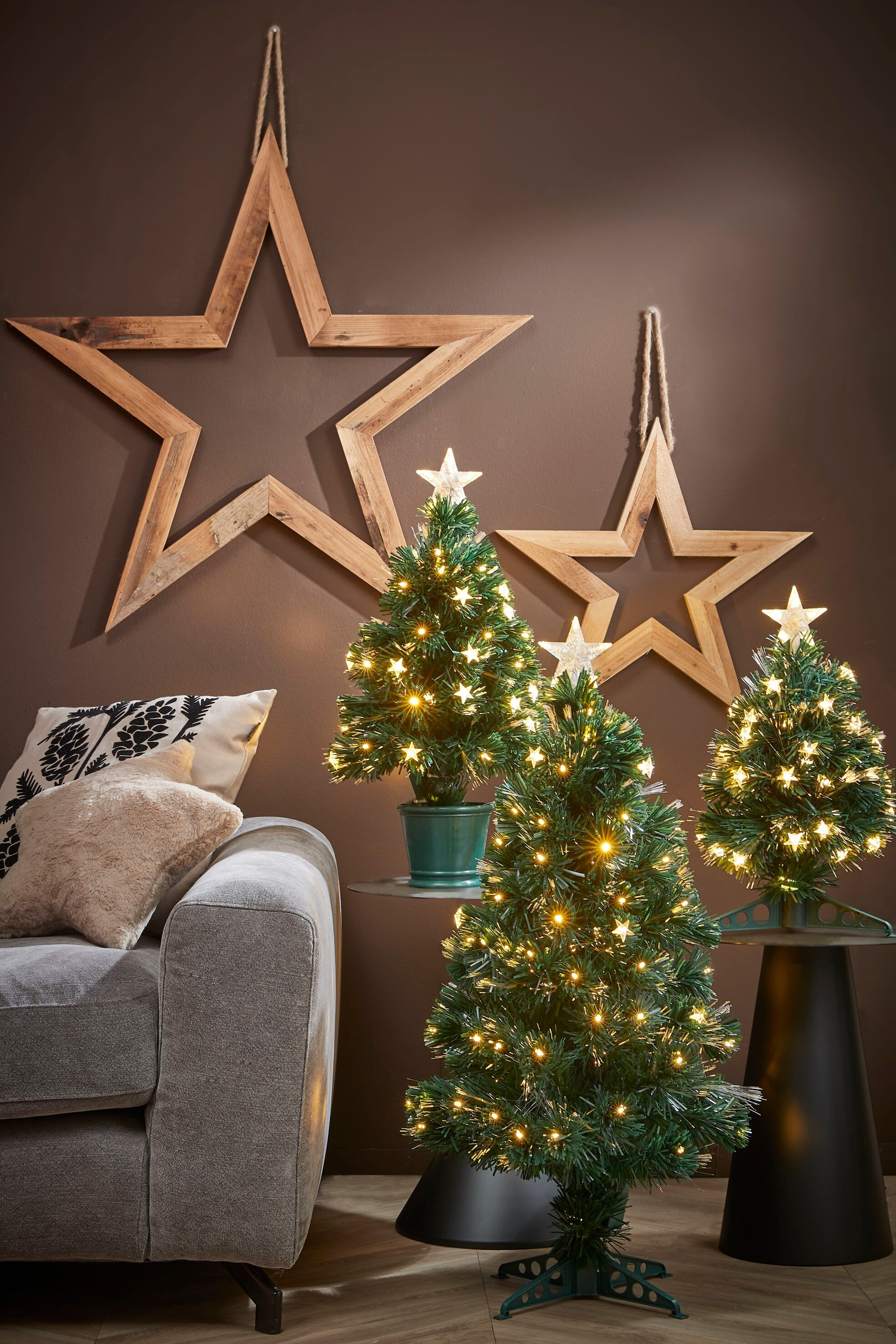 Salon avec sapins de Noël, décorations d'étoiles, un canapé et des oreillers. Les arbres ont des lumières et des étoiles.