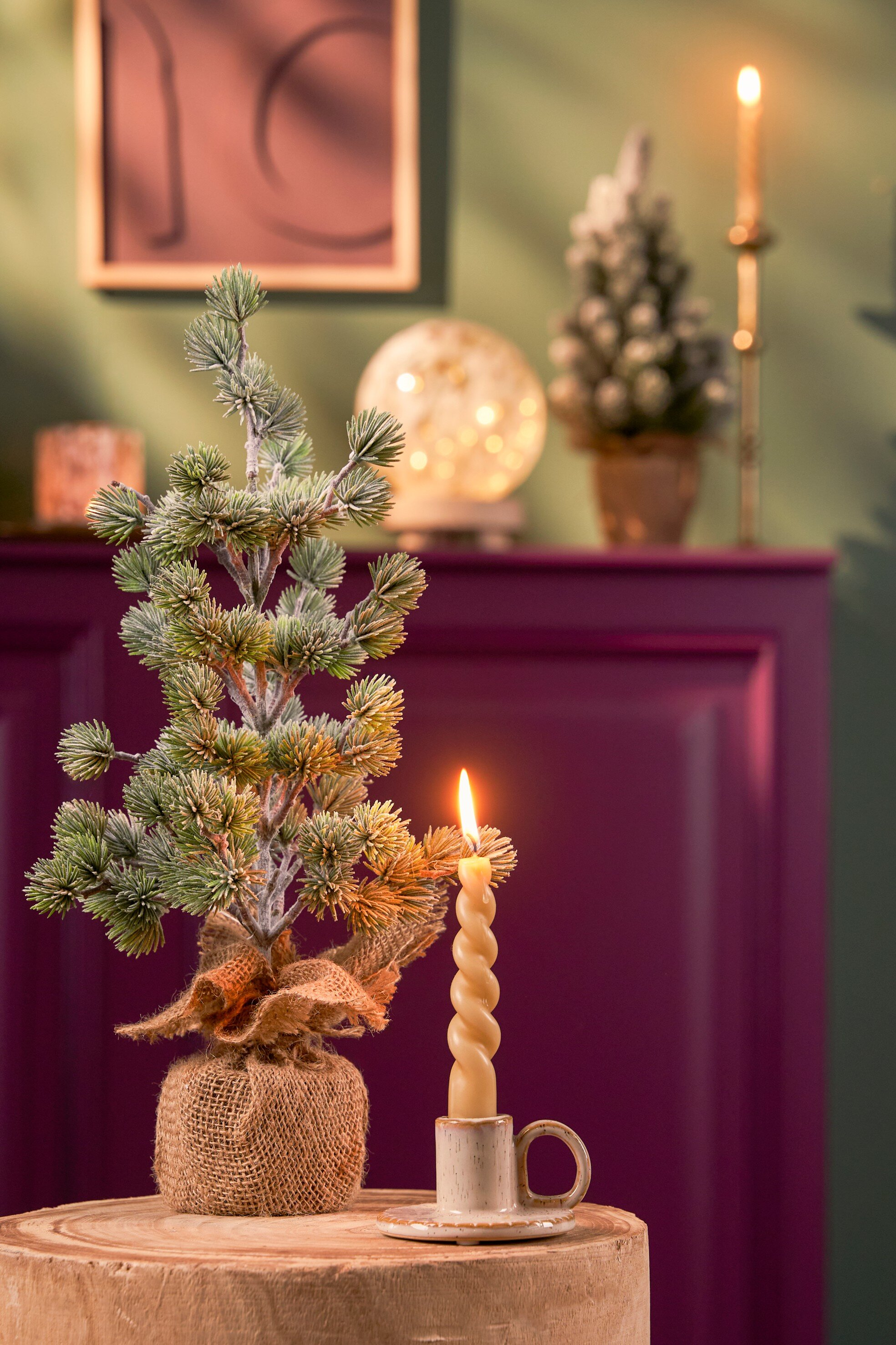 Une bougie allumée et un petit sapin de Noël sont sur une surface en bois. Mur rouge foncé en arrière-plan.