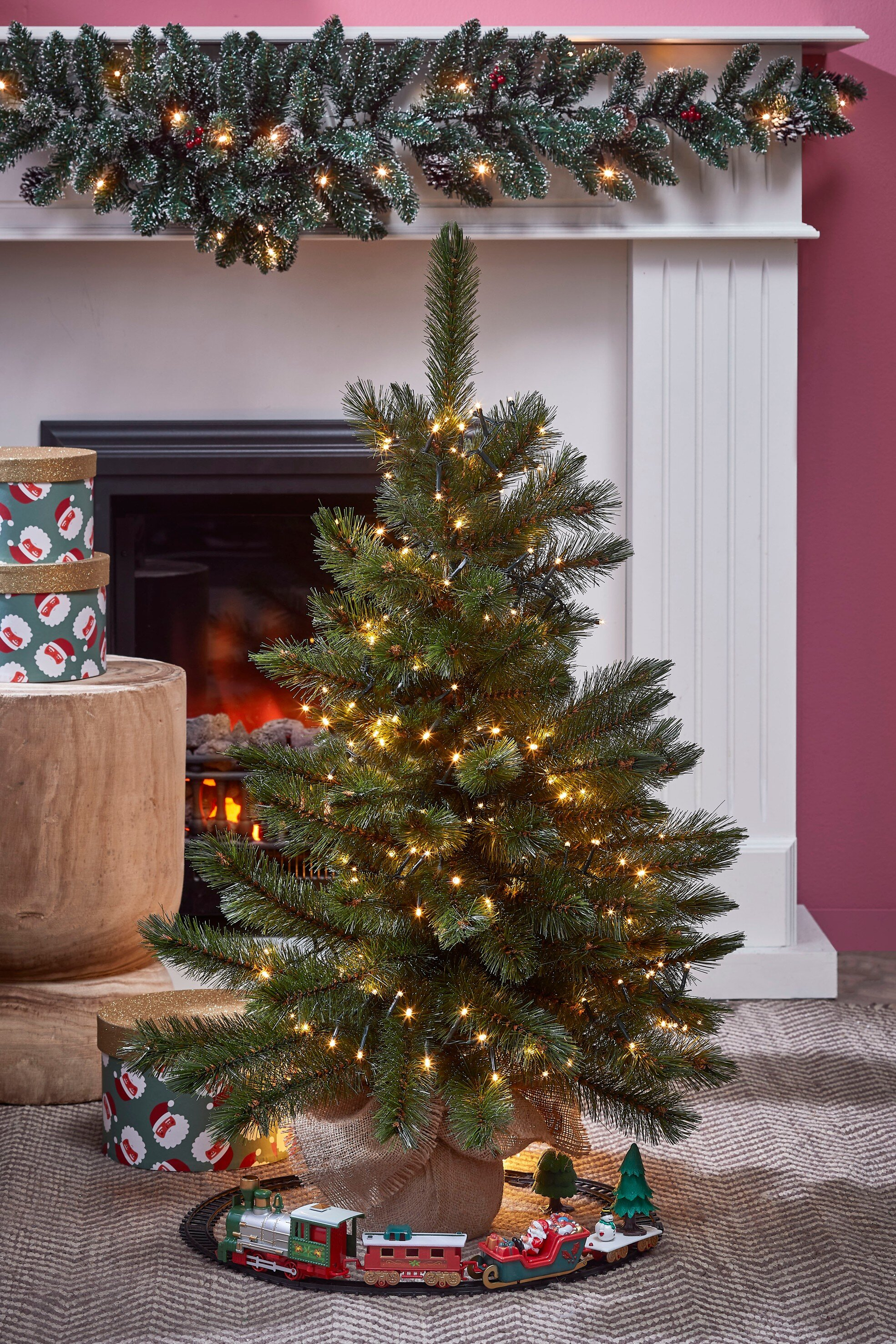 Un sapin de Noël décoré avec des lumières, un train jouet et des cadeaux, devant une cheminée.