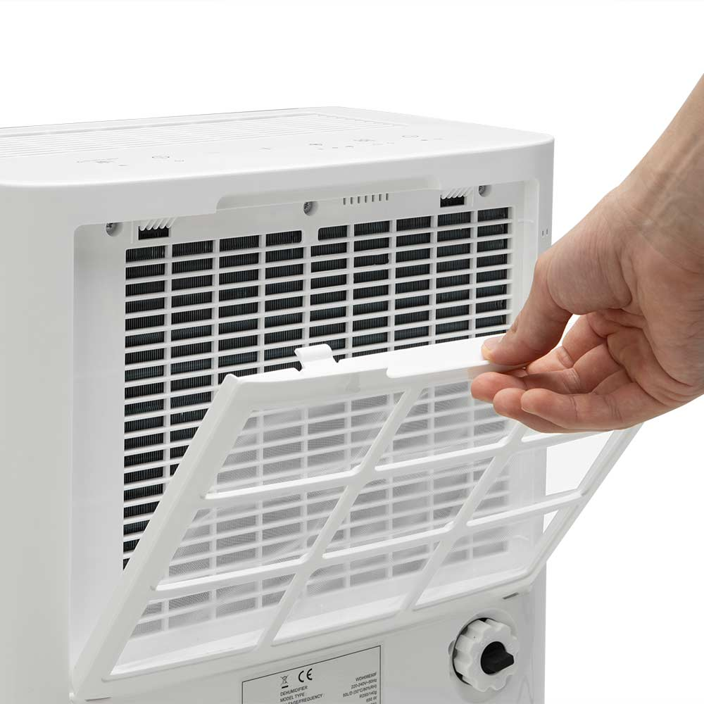Una mano abre un filtro de aire blanco en un deshumidificador blanco. El filtro es rectangular con un patrón de rejilla.