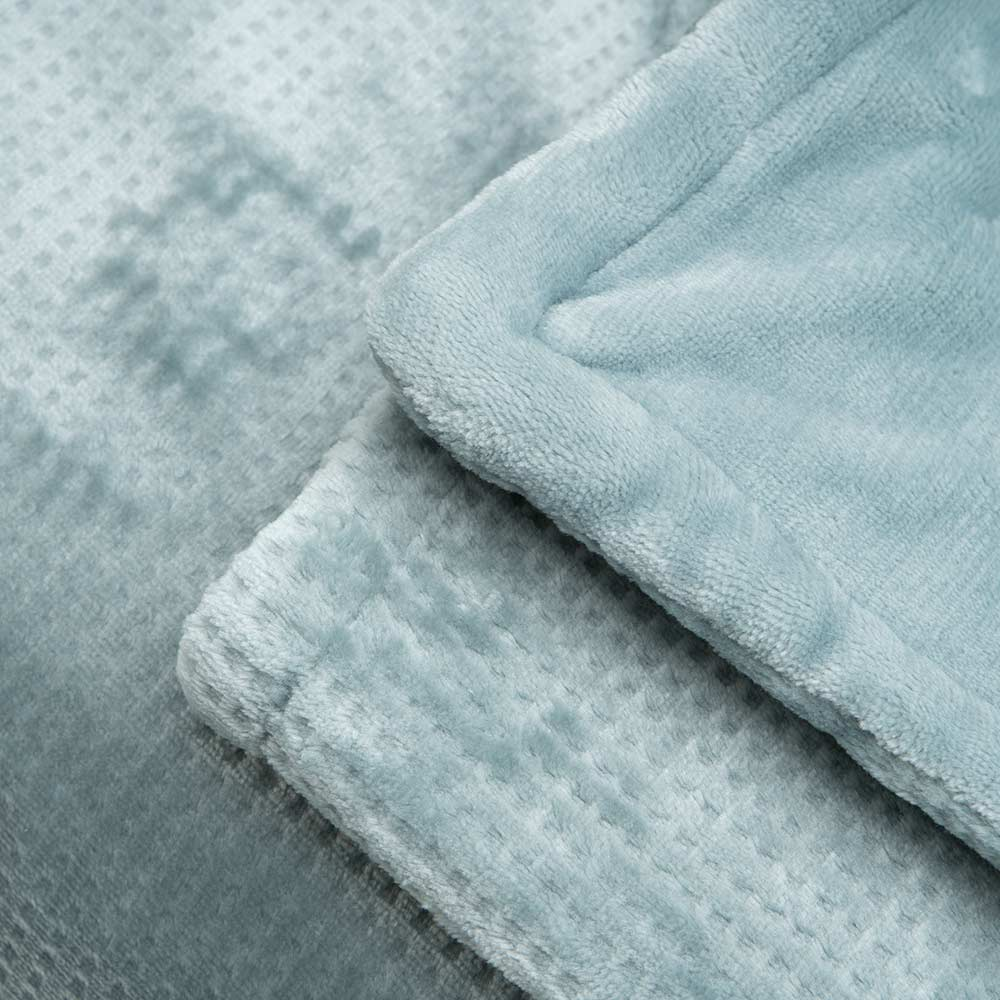 Primer plano de una manta azul claro doblada. La manta tiene una textura afelpada con un patrón acolchado y un borde suave.