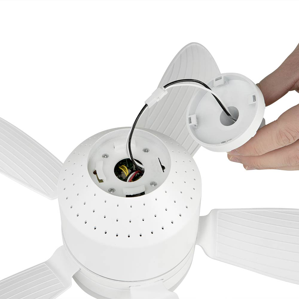 Se está montando un ventilador de techo blanco. Una mano sostiene una cubierta separada, con cables expuestos. Las aspas del ventilador también son blancas.