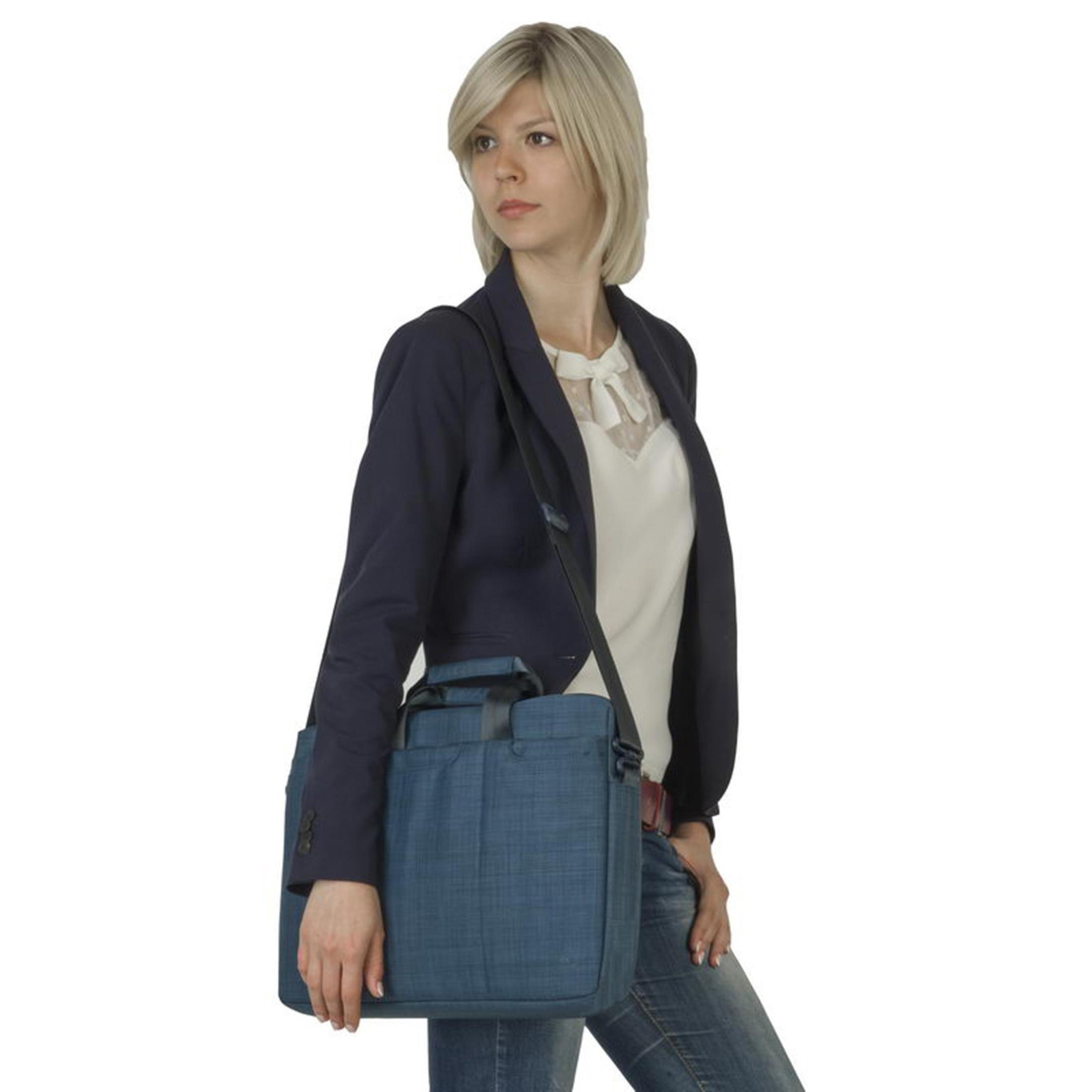 Una donna con un blazer blu navy porta una borsa blu sulla spalla. Indossa un top bianco e jeans.