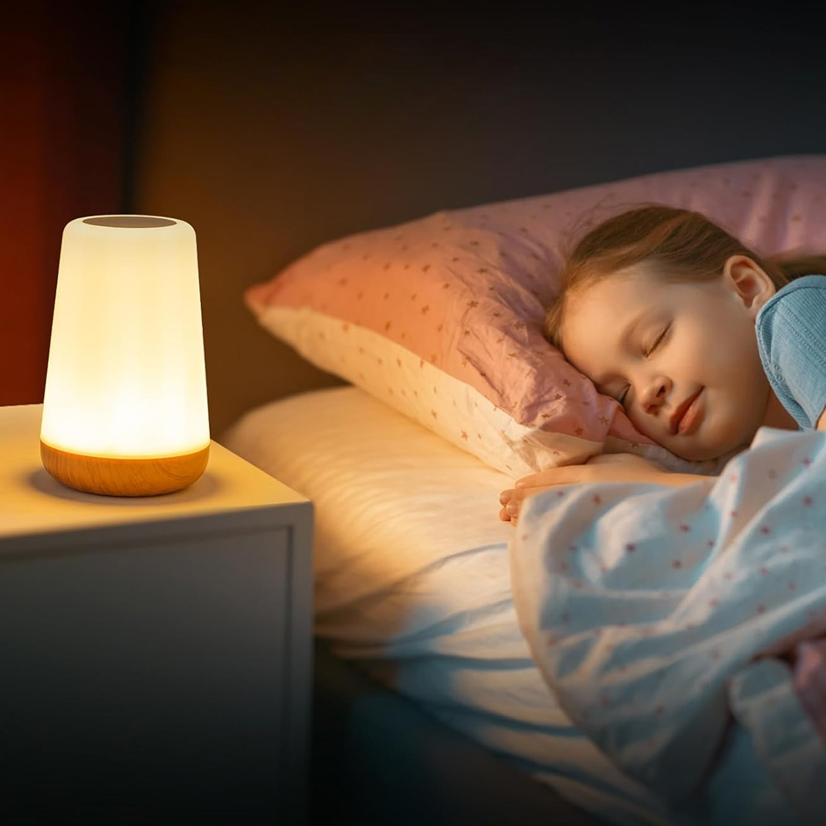 Ein schlafendes Mädchen im Bett. Eine beleuchtete Lampe steht auf einem Nachttisch. Rosa Kissen und Decke. Warme Beleuchtung.
