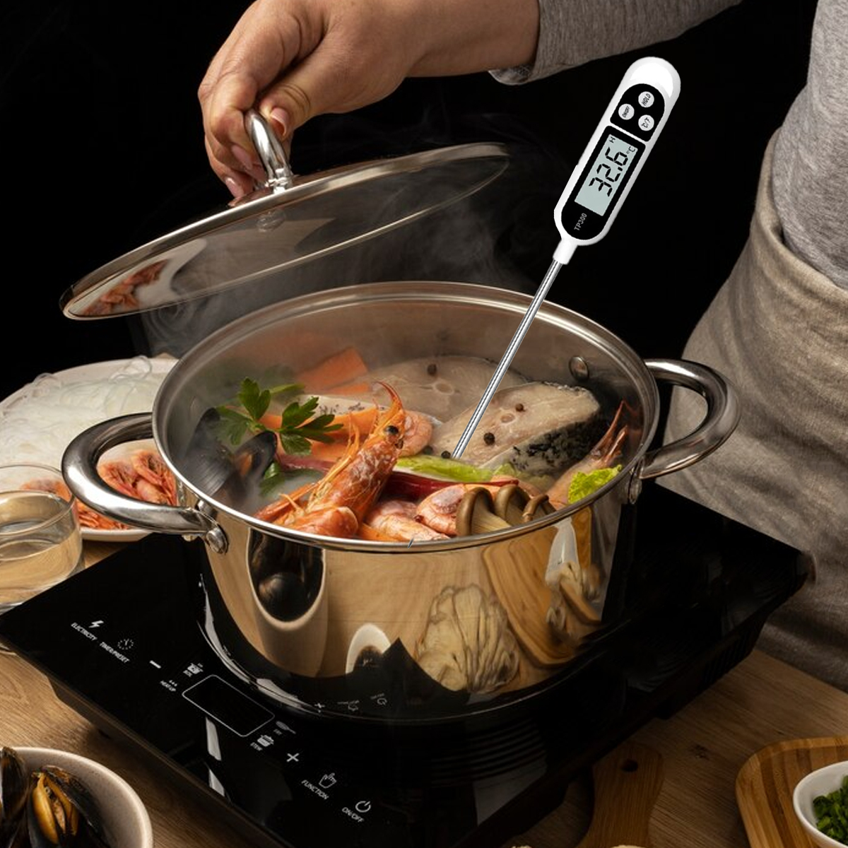 Ein Topf mit Meeresfrüchtesuppe mit Thermometer. Eine Hand hebt den Deckel. Die Suppe enthält Garnelen, Fisch und Gemüse.