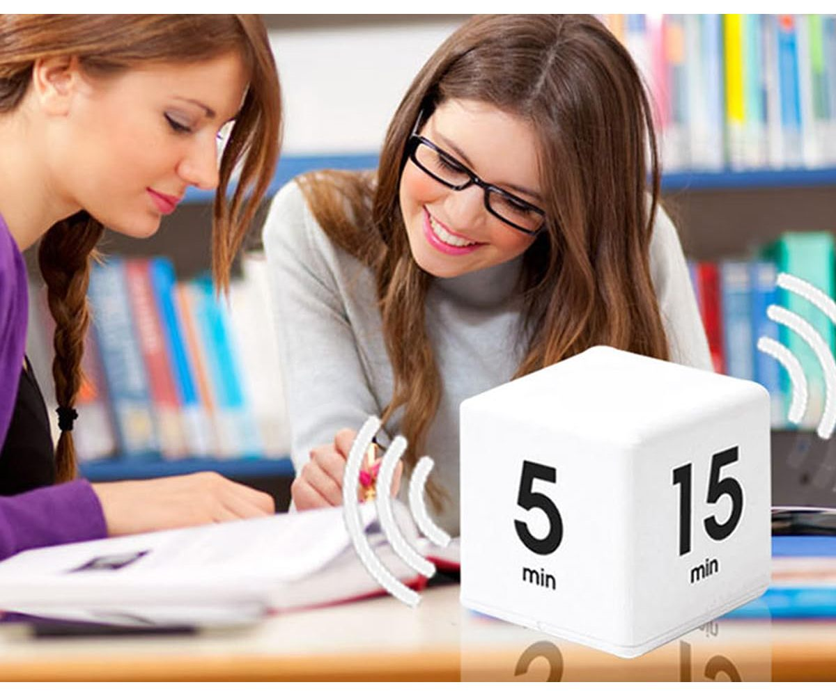 Zwei Frauen lernen, eine trägt eine Brille. Ein weißer Würfel-Timer zeigt '5 min' und '15 min'. Bücherregale im Hintergrund.