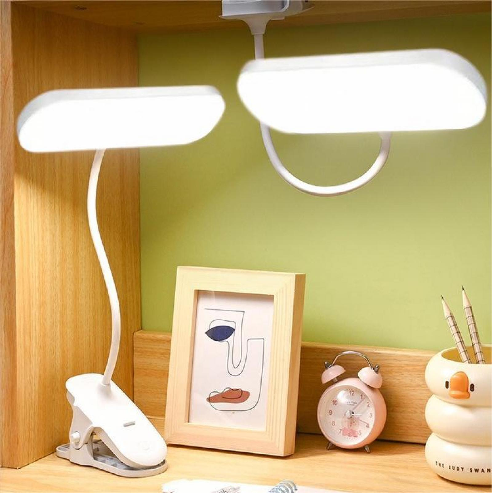 Zwei weiße Schreibtischlampen beleuchten eine Szene mit einem Bild, einem Wecker, Bleistiften und einem Enten-Stifthalter.
