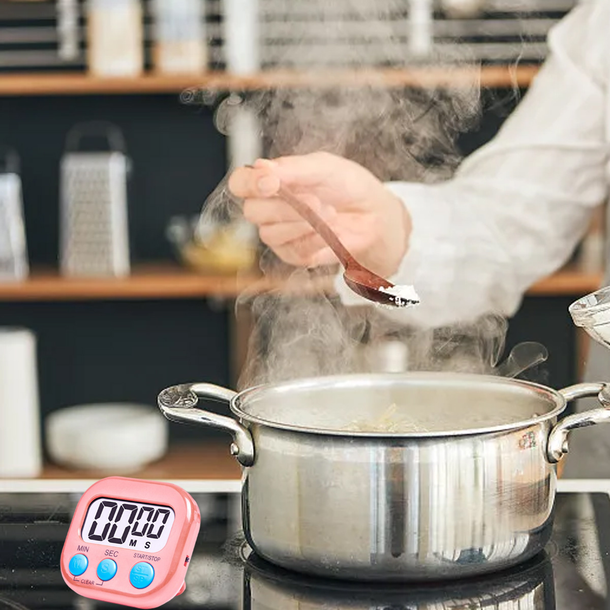 Eine Person fügt Salz in kochendes Wasser in einem Topf hinzu. Im Vordergrund befindet sich ein rosa Timer. Dampf steigt auf. Ein Holzlöffel wird verwendet.