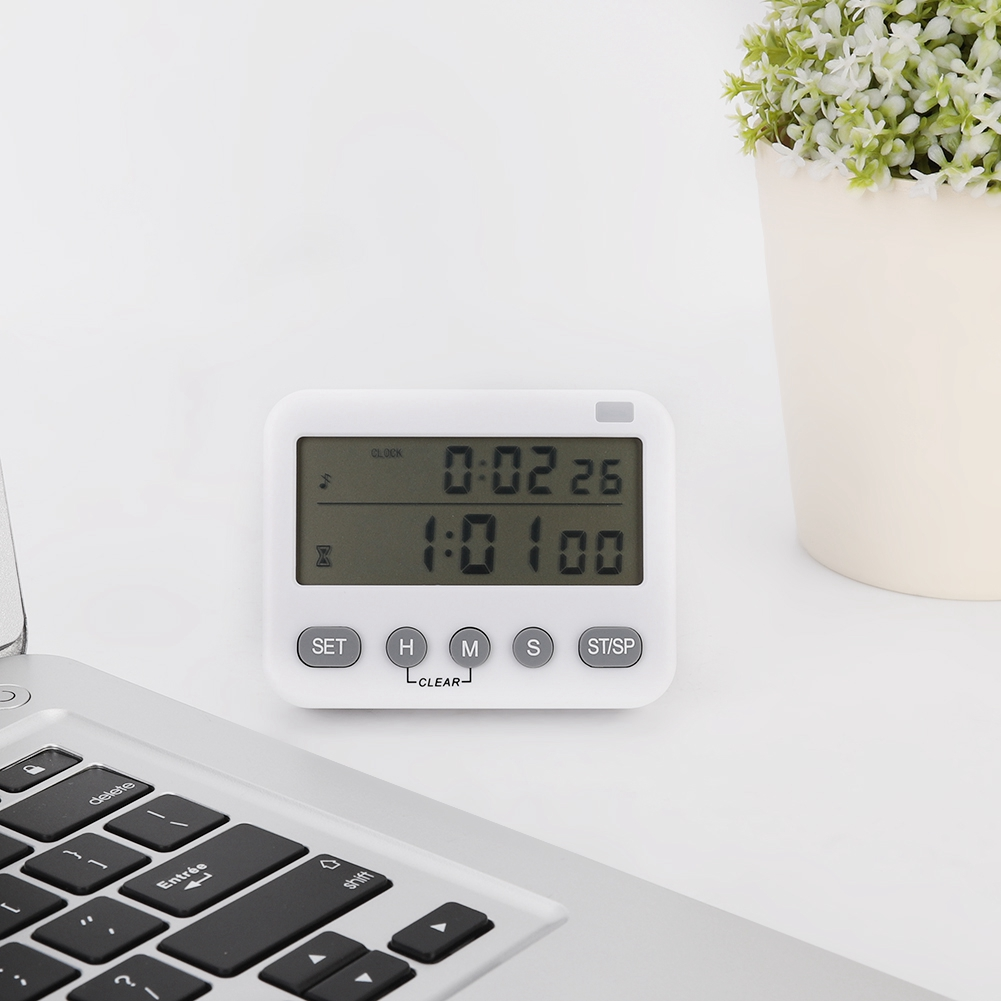 Ein weißer Timer zeigt 0:02:26 und 1:01:00. Er liegt auf einer weißen Oberfläche mit einem Laptop und einer Topfpflanze im Hintergrund.