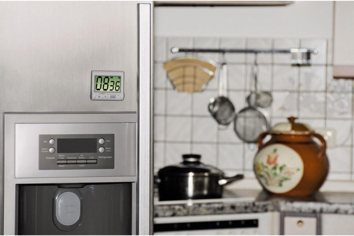 Kühlschrank mit Timer, der 08:36 anzeigt. Küchenhintergrund: Töpfe, Pfannen und ein dekorativer Topf auf der Theke.