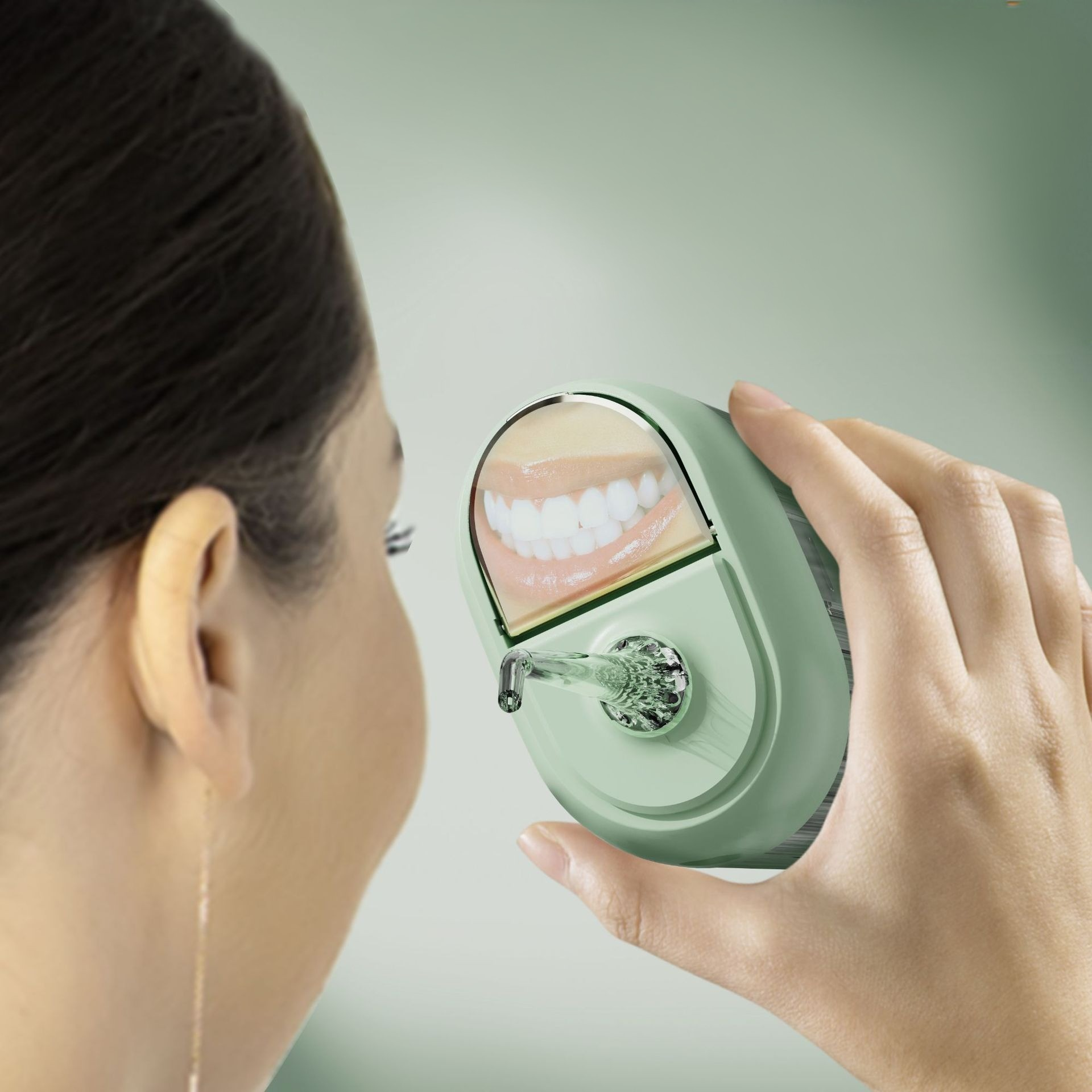 Eine Frau betrachtet einen grünen Dental-Irrigator, der Zähne zeigt. Das Gerät wird in der Hand gehalten, und die Szene ist vor hellem Hintergrund.