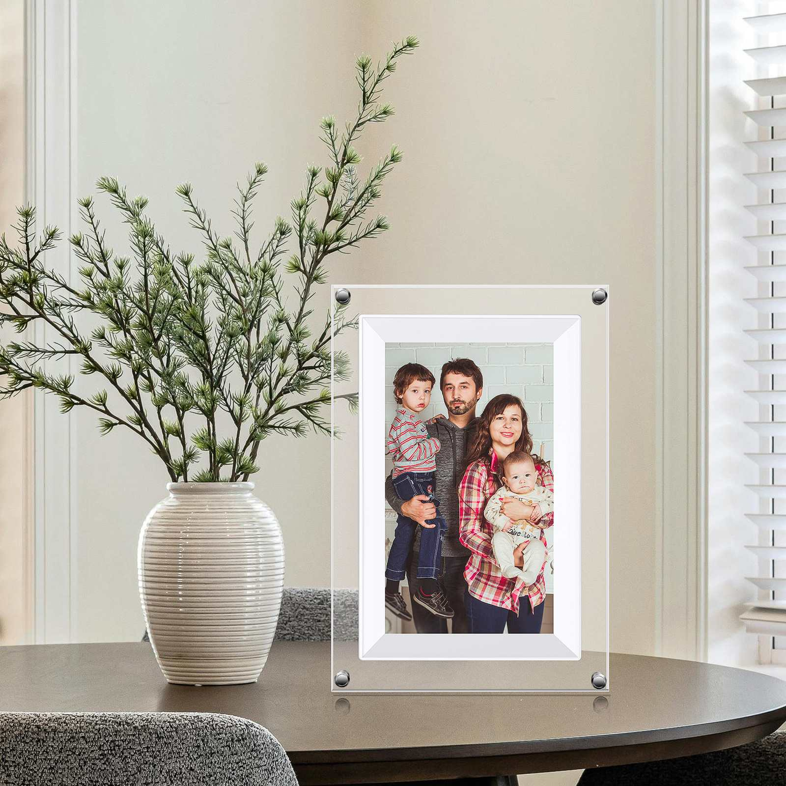 Ein Familienporträt in einem Rahmen. Auf dem Tisch steht eine Vase mit grünen Pflanzen. Im Hintergrund ist ein Fenster.