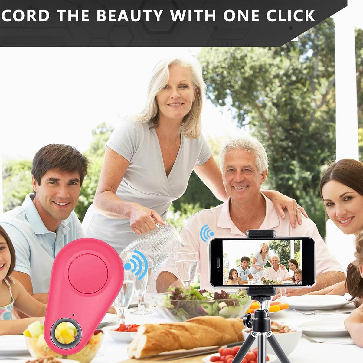 Familie am Tisch mit Essen, macht ein Foto mit einem Smartphone auf einem Stativ. Eine rosa Fernbedienung ist im Vordergrund.