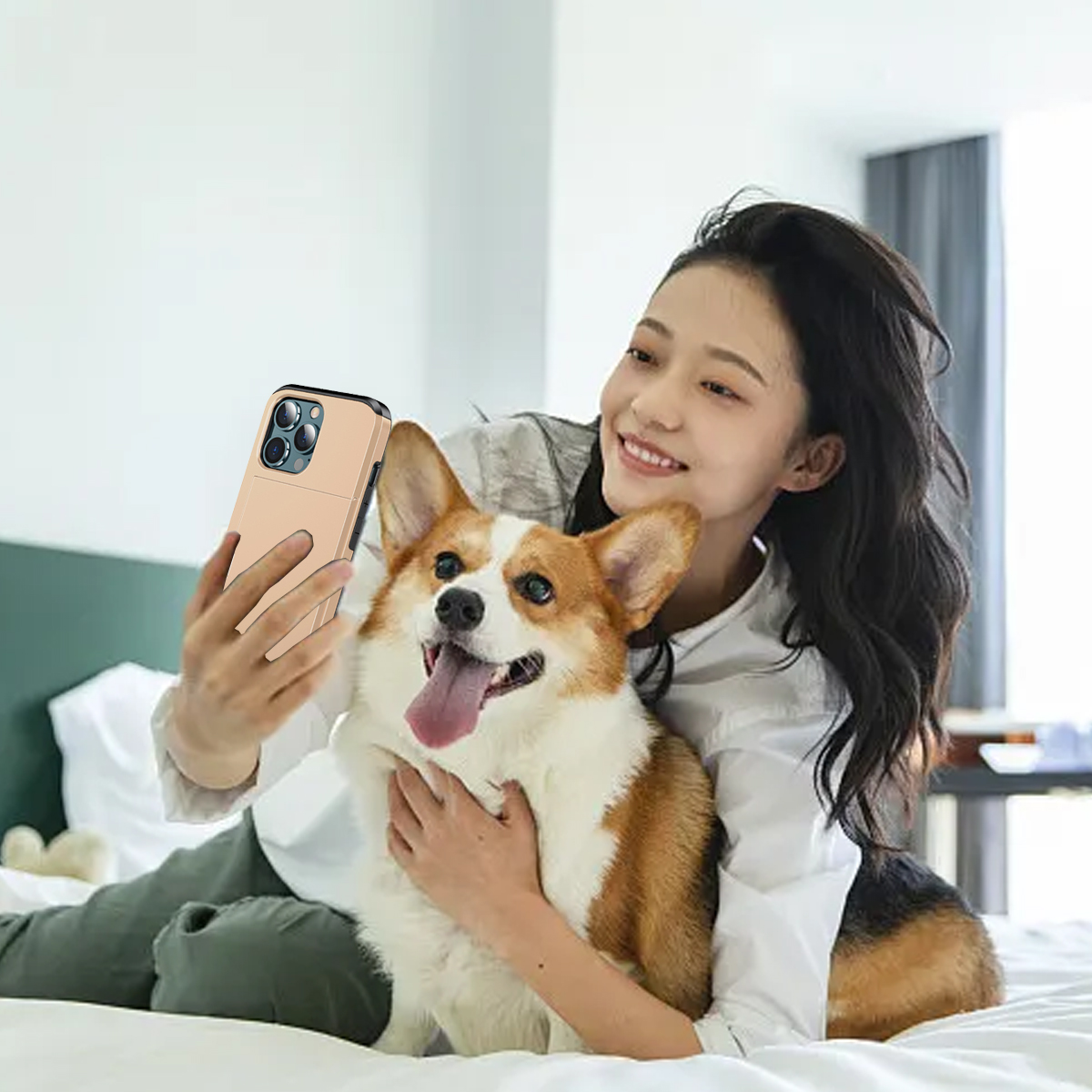 Eine Frau macht ein Selfie mit einem Corgi-Hund. Beide sind auf einem Bett. Der Hund hat die Zunge draußen. Die Frau hält ein Telefon.