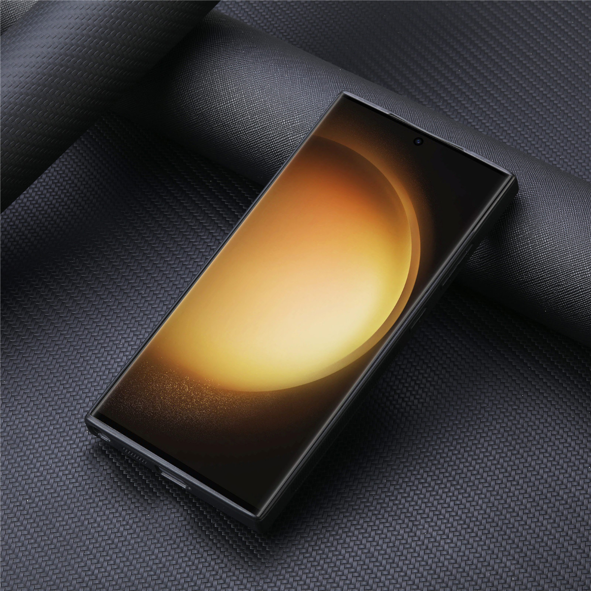Ein Smartphone mit goldenem Display liegt auf einer strukturierten schwarzen Oberfläche. Das Telefon ist schwarz und hat eine Kamera.