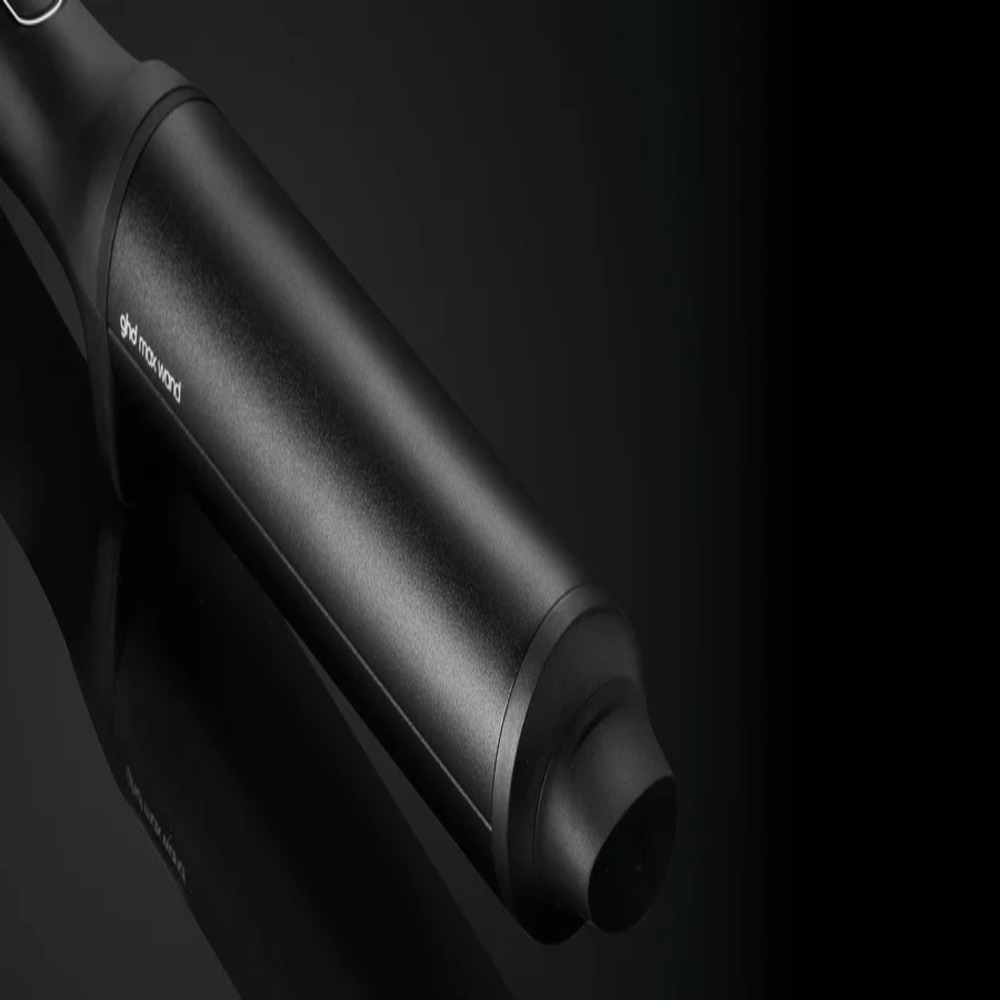 Nahaufnahme eines schwarzen ghd max Wand-Lockenstabs auf einer reflektierenden schwarzen Oberfläche. Das Werkzeug ist abgewinkelt, mit 'ghd max wand' sichtbar.