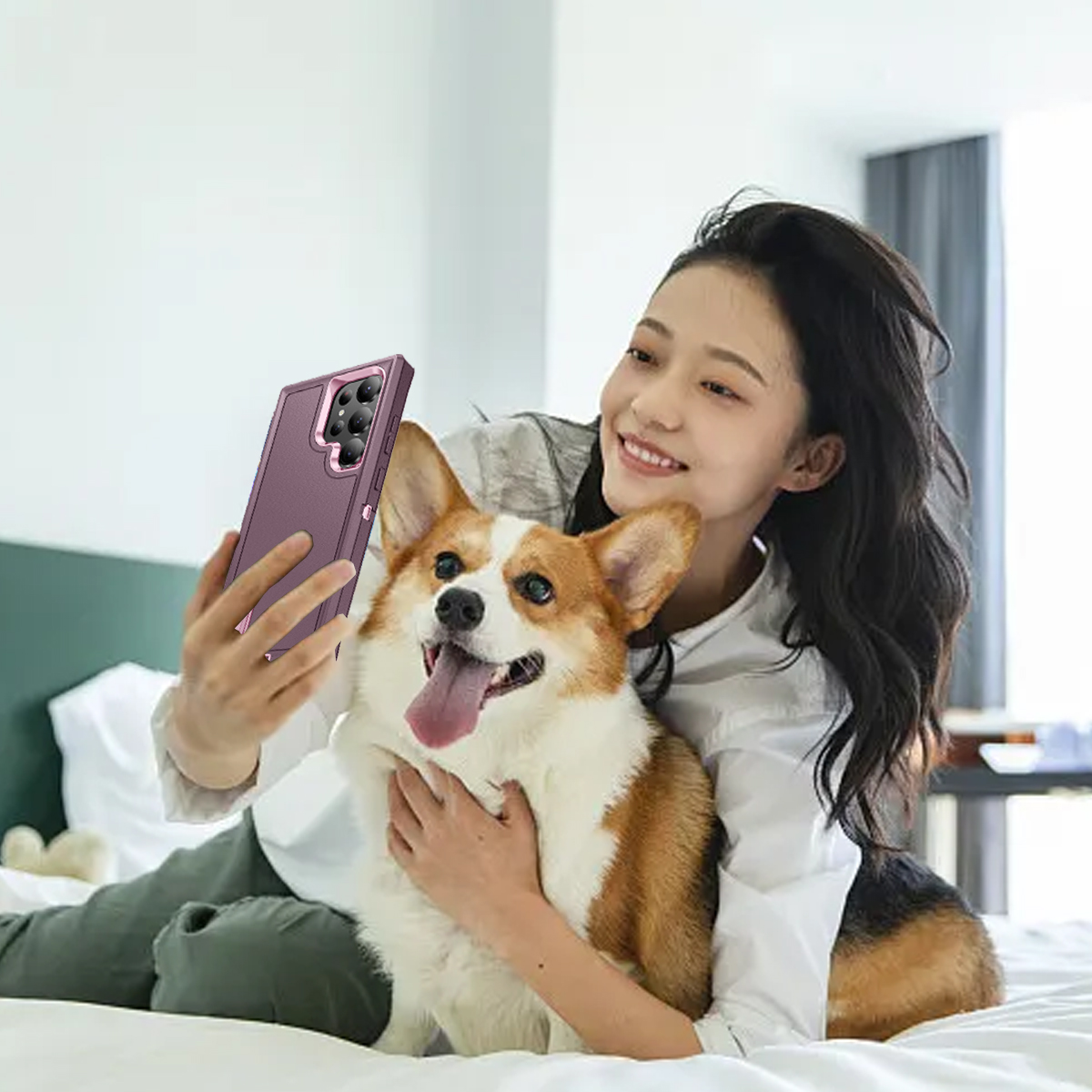 Eine Frau macht ein Selfie mit einem Corgi-Hund. Beide sind auf einem Bett. Der Hund hat die Zunge draußen. Das Telefon hat eine lila Hülle.