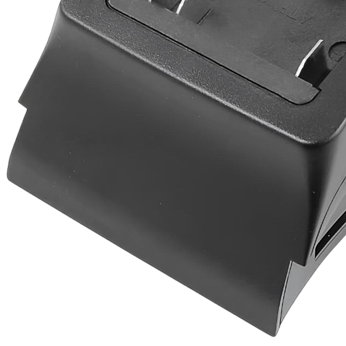 Nahaufnahme eines schwarzen Plastikgeräts, möglicherweise ein Ladegerät oder eine Basis, mit abgewinkelten Seiten und einer strukturierten Oberseite. Weißer Hintergrund.