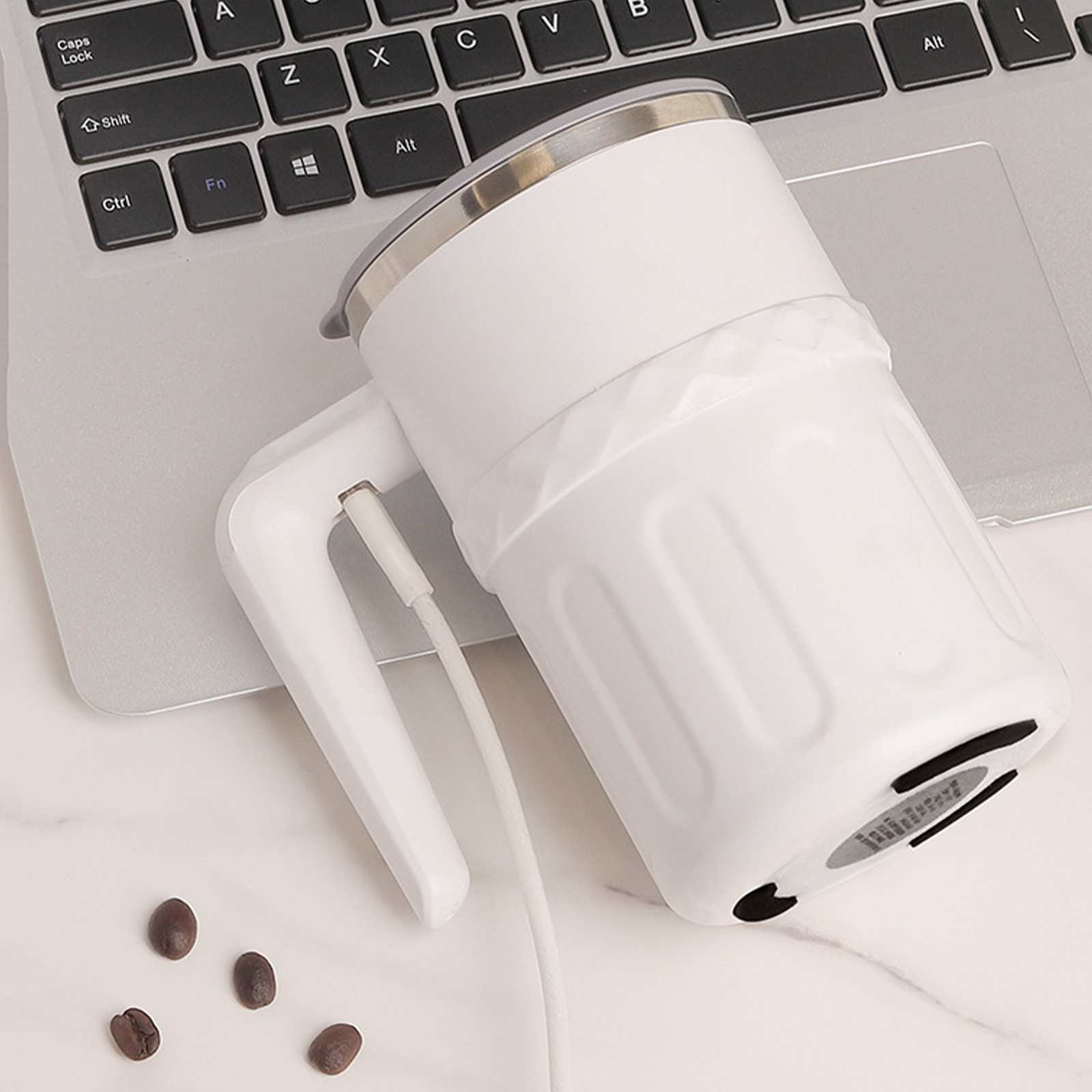 Weißer Becher mit Griff, eingesteckt, auf einem Laptop. Kaffeebohnen sind auf dem Tisch verstreut.