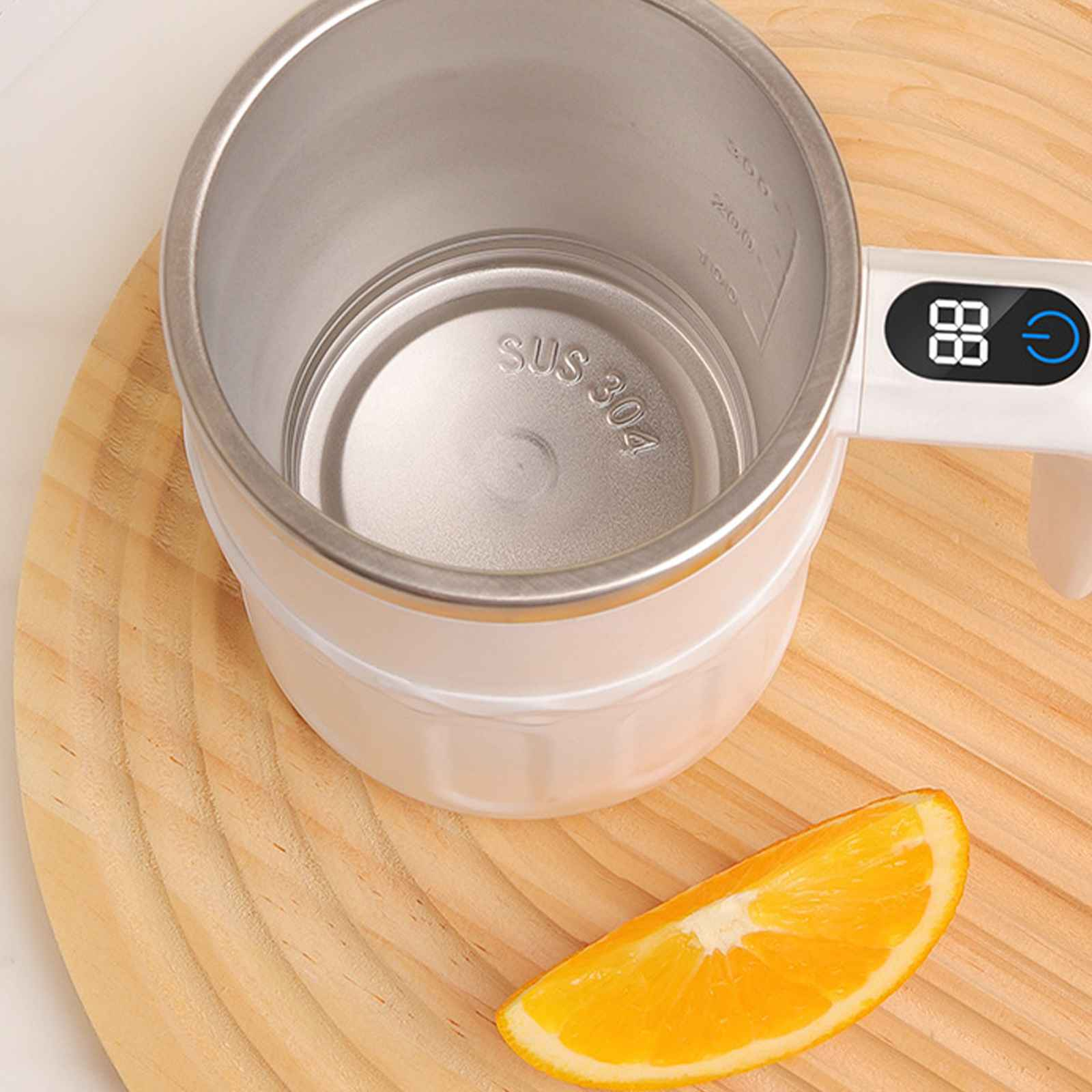 Ein weißer und silberner Wasserkocher mit digitaler Anzeige und einer Orangenscheibe auf einem Holzbrett.
