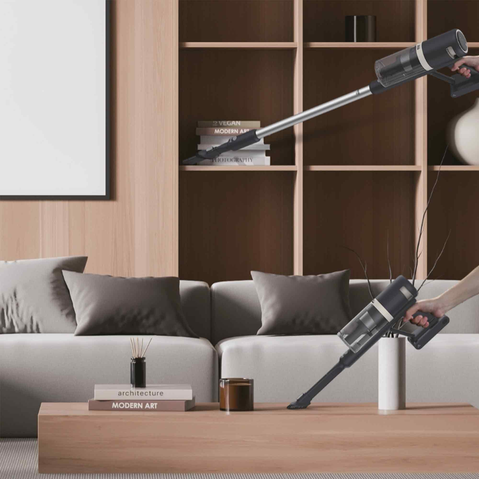 Un salon moderne avec un aspirateur en cours d'utilisation. Un canapé blanc, des étagères en bois et une table basse sont visibles.