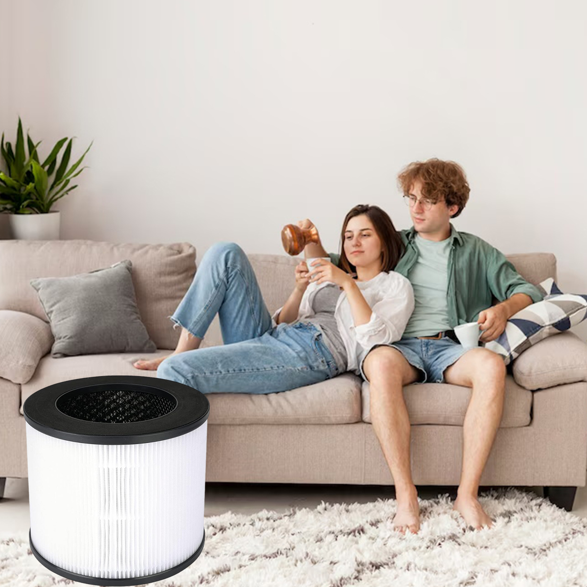 Ein Paar entspannt sich auf einem Sofa, einer gießt Flüssigkeit in eine Tasse. Ein Luftfilter steht im Vordergrund. Links ist eine Pflanze.