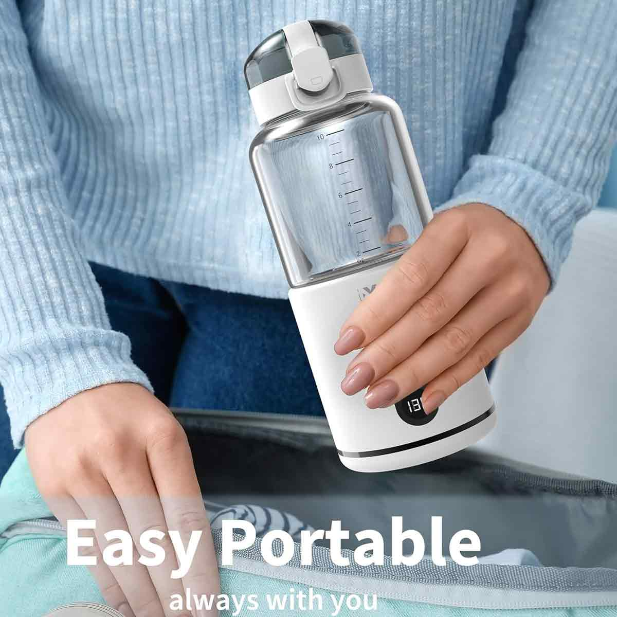 Eine Person hält einen weißen und durchsichtigen tragbaren Mixer. Der Hintergrund umfasst einen hellblauen Pullover und eine Tasche.