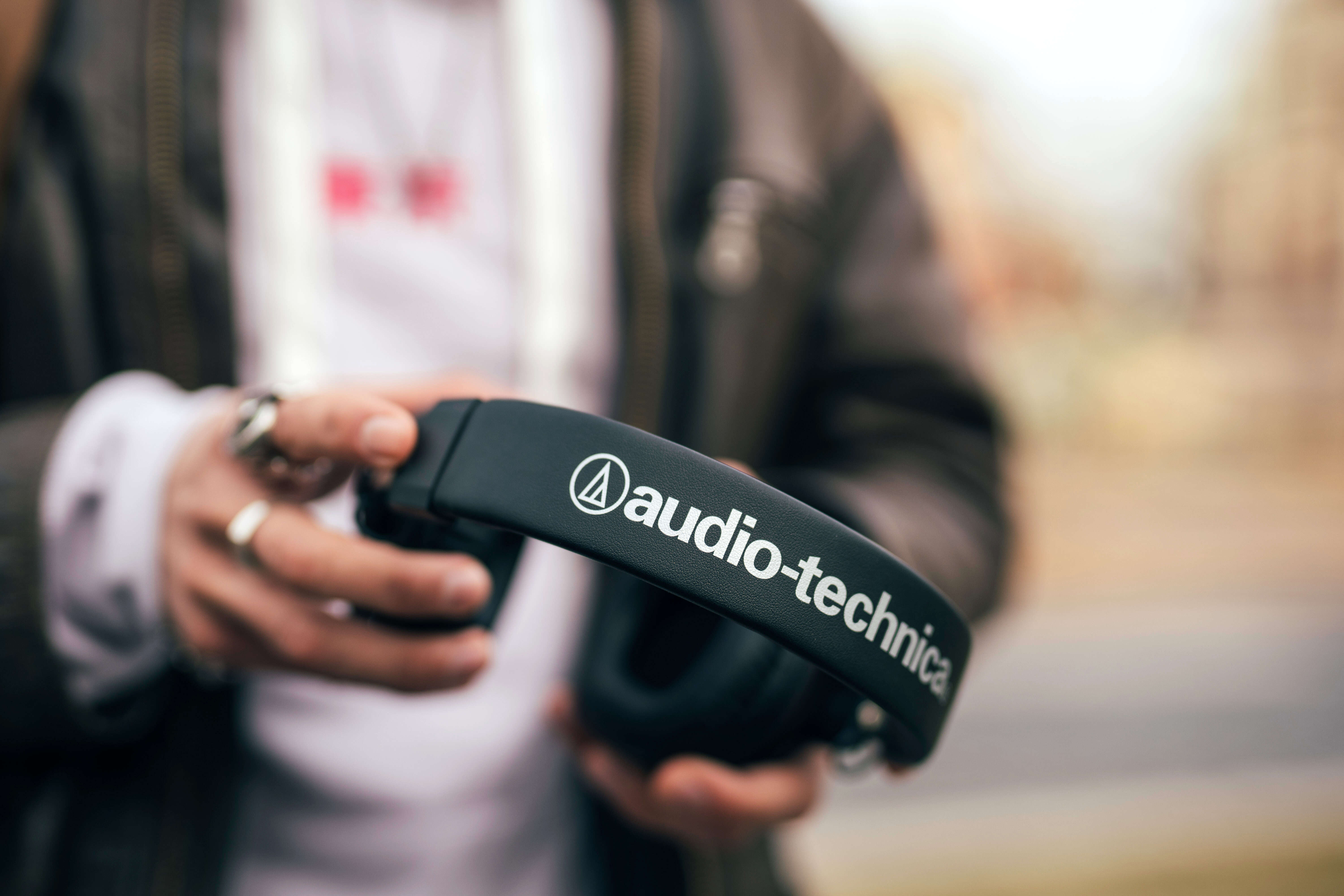Osoba trzyma czarne słuchawki Audio-Technica. Logo jest widoczne. Tło jest rozmyte.